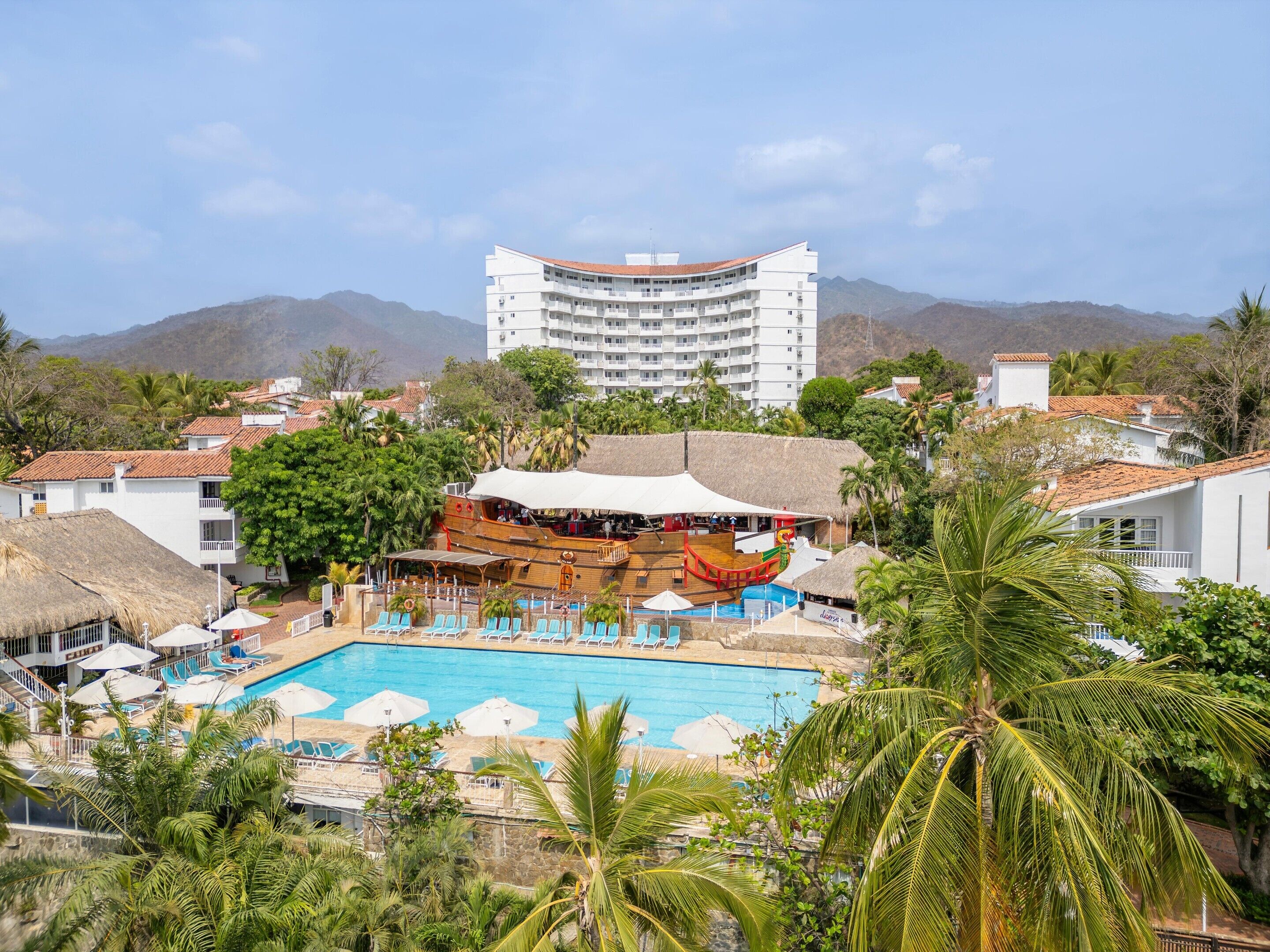 A resort with a swimming pool, a wooden boat, and a mountain backdrop.
