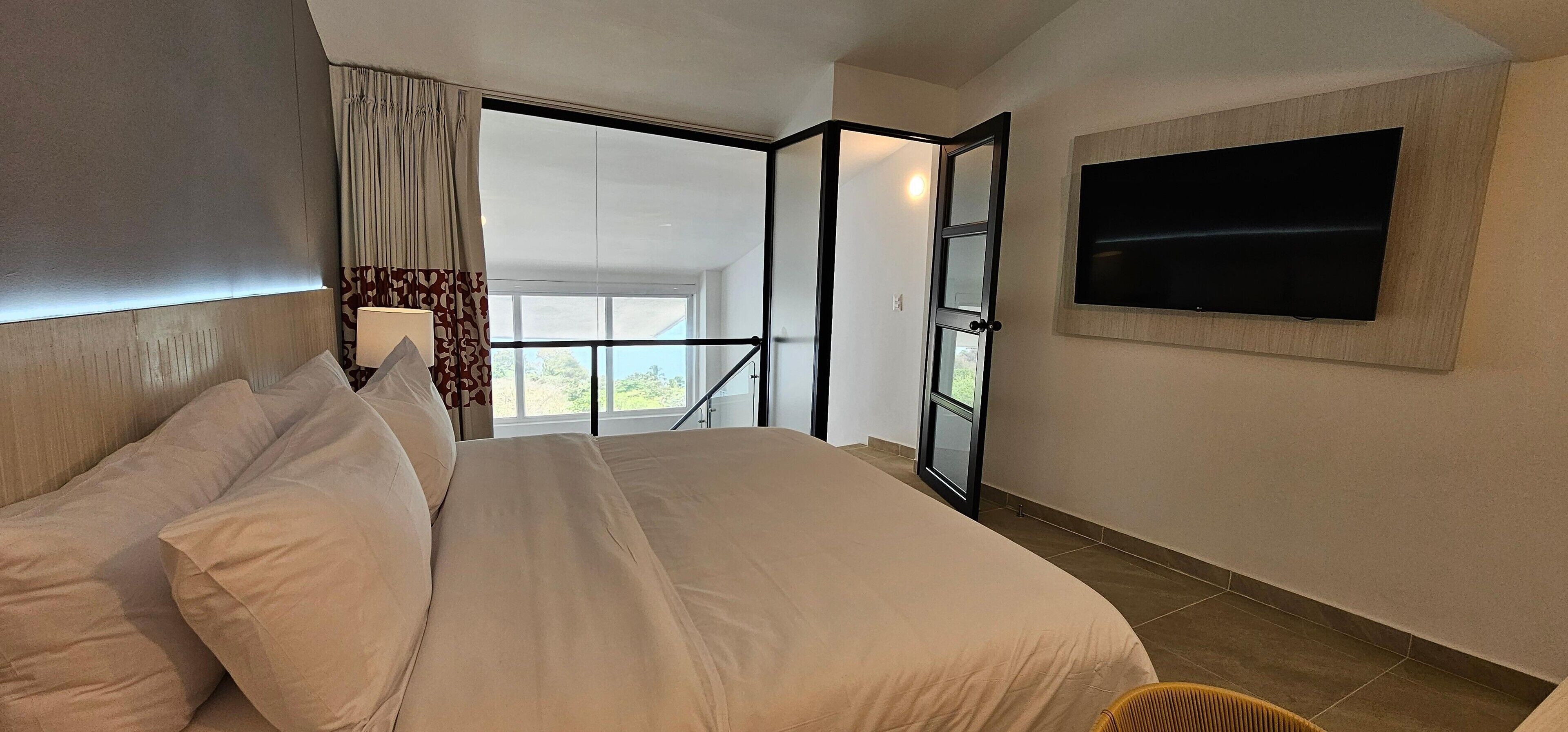 Ein Hotelzimmer mit einem Bett, einem an der Wand montierten Fernseher und Blick durch eine Glastür.
