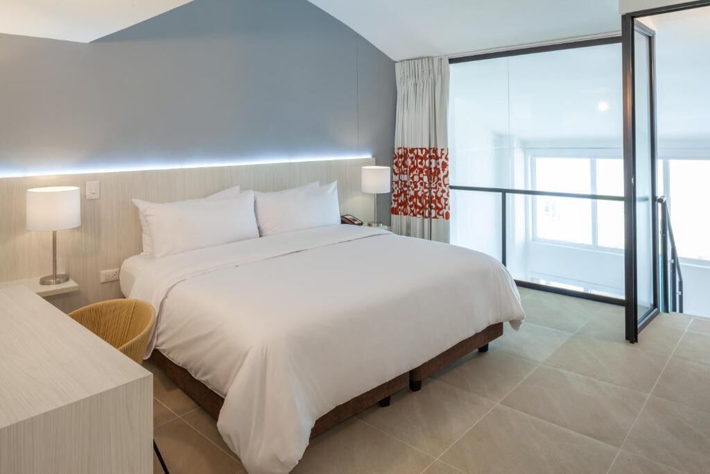Habitación de hotel moderna con una cama grande, lámparas de noche, un escritorio y vistas al exterior.
