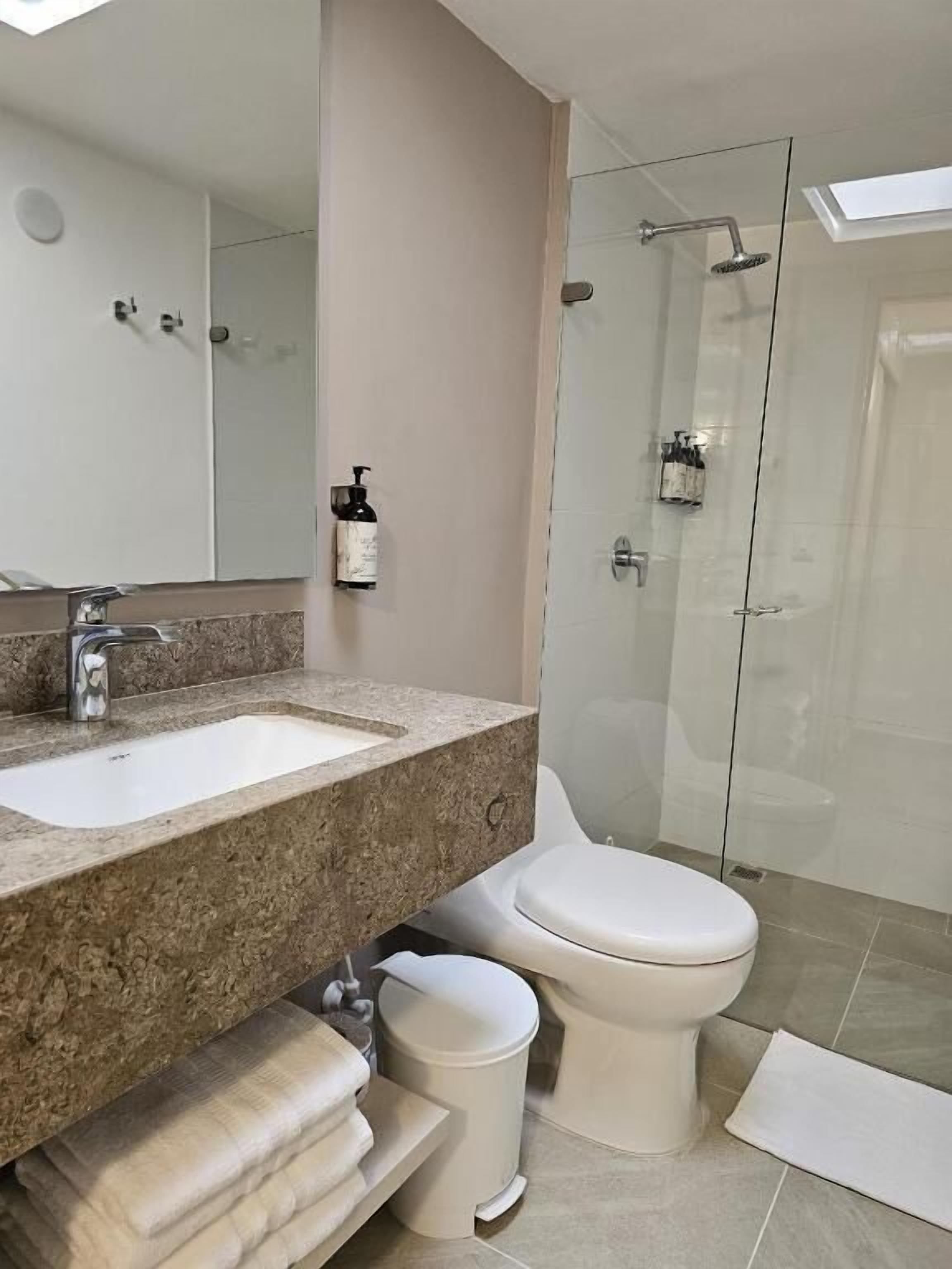 Un baño con lavamanos de mármol, inodoro, cabina de ducha de vidrio y espejo.