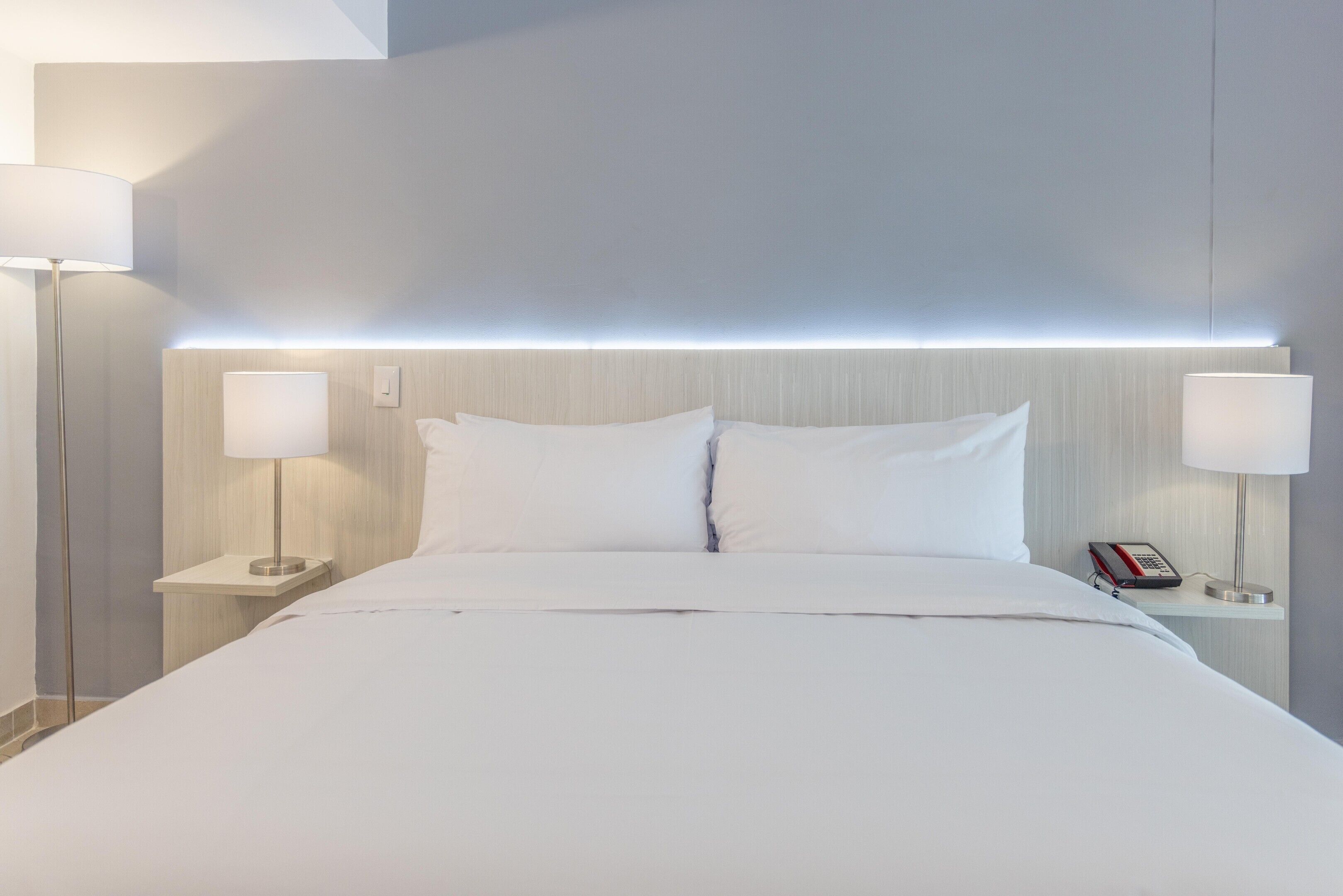 Ein modernes Hotelzimmer mit einem großen Bett, zwei Nachttischen und einem Kopfteil mit integrierter Beleuchtung.