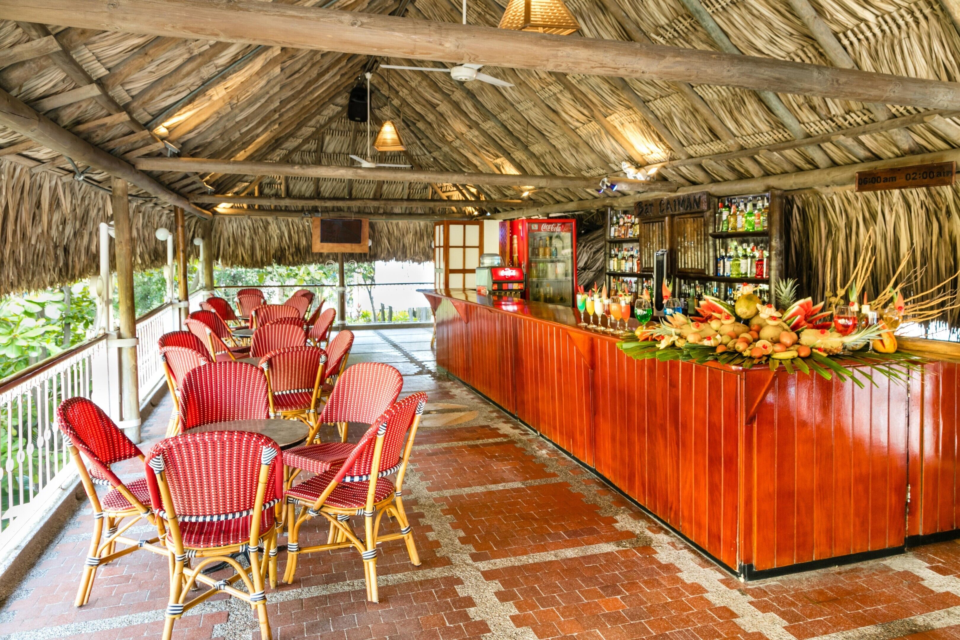 A bar area with a wooden counter, red wicker chairs, and a thatched roof.