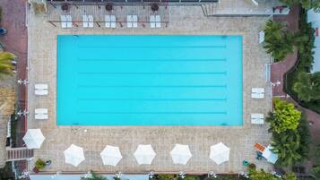 An aerial view of a swimming pool with lanes, surrounded by white umbrellas and lounge chairs.