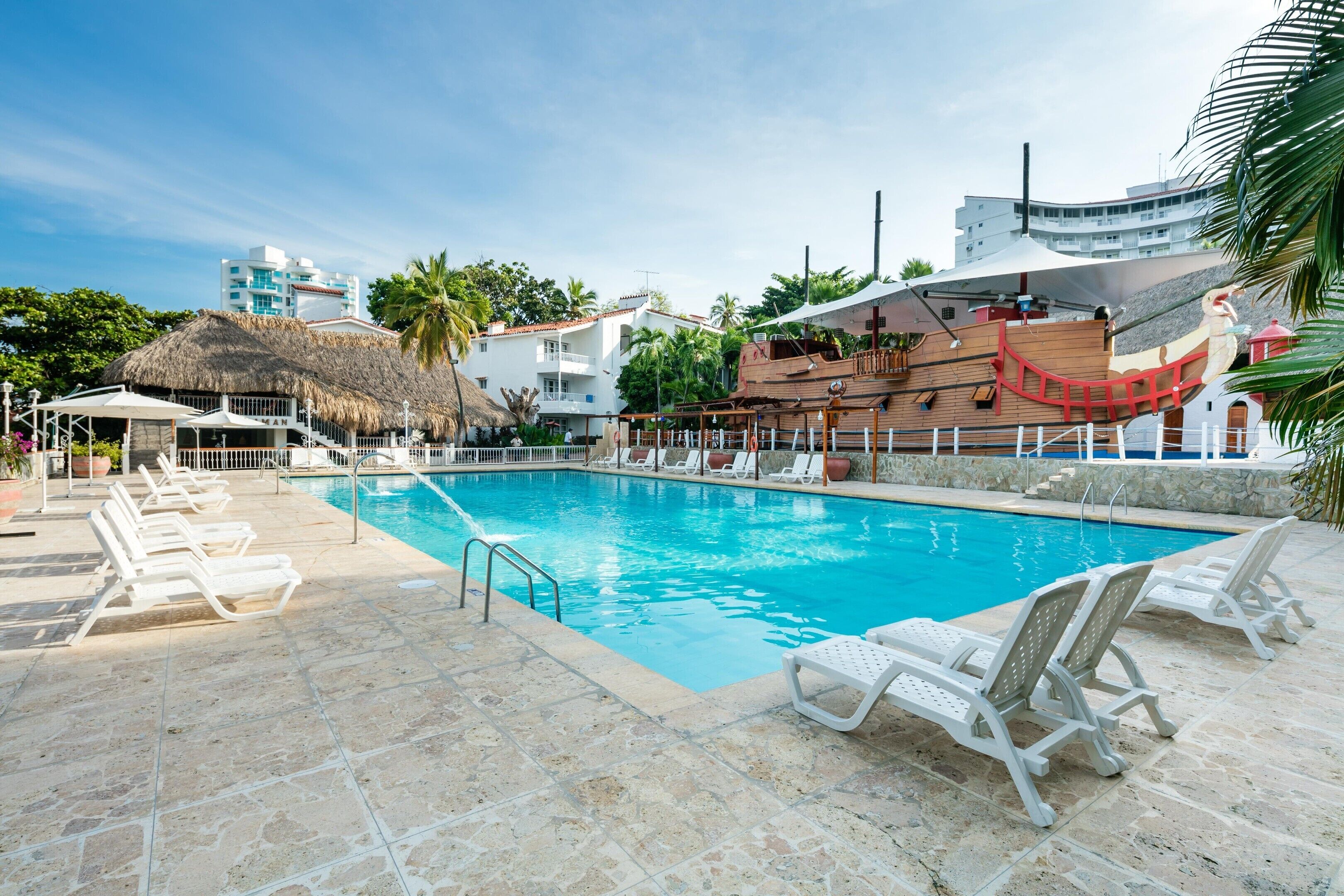 A swimming pool with lounge chairs, a thatched-roof structure, and a wooden boat model.