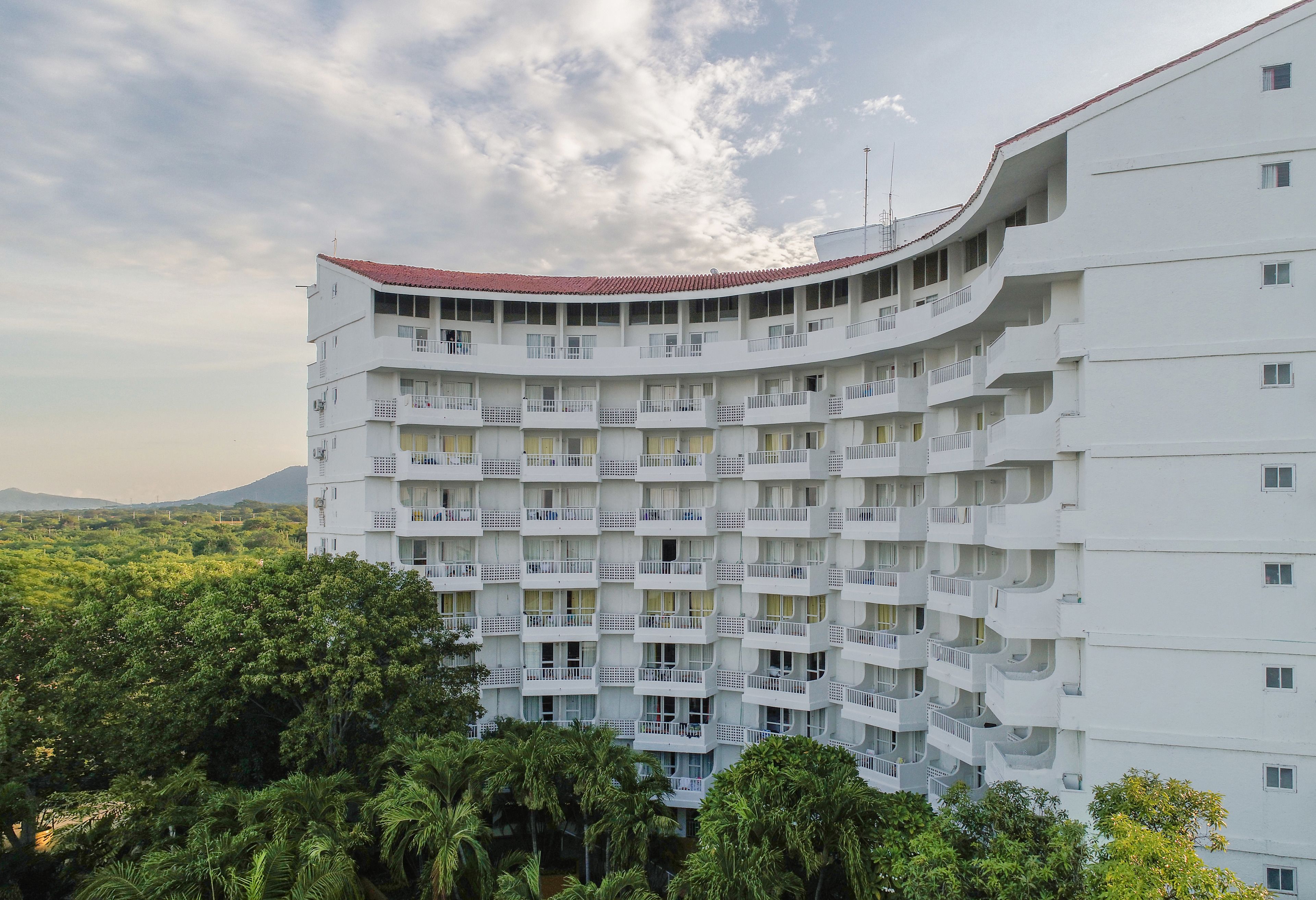 A multi-story building with balconies, surrounded by greenery.