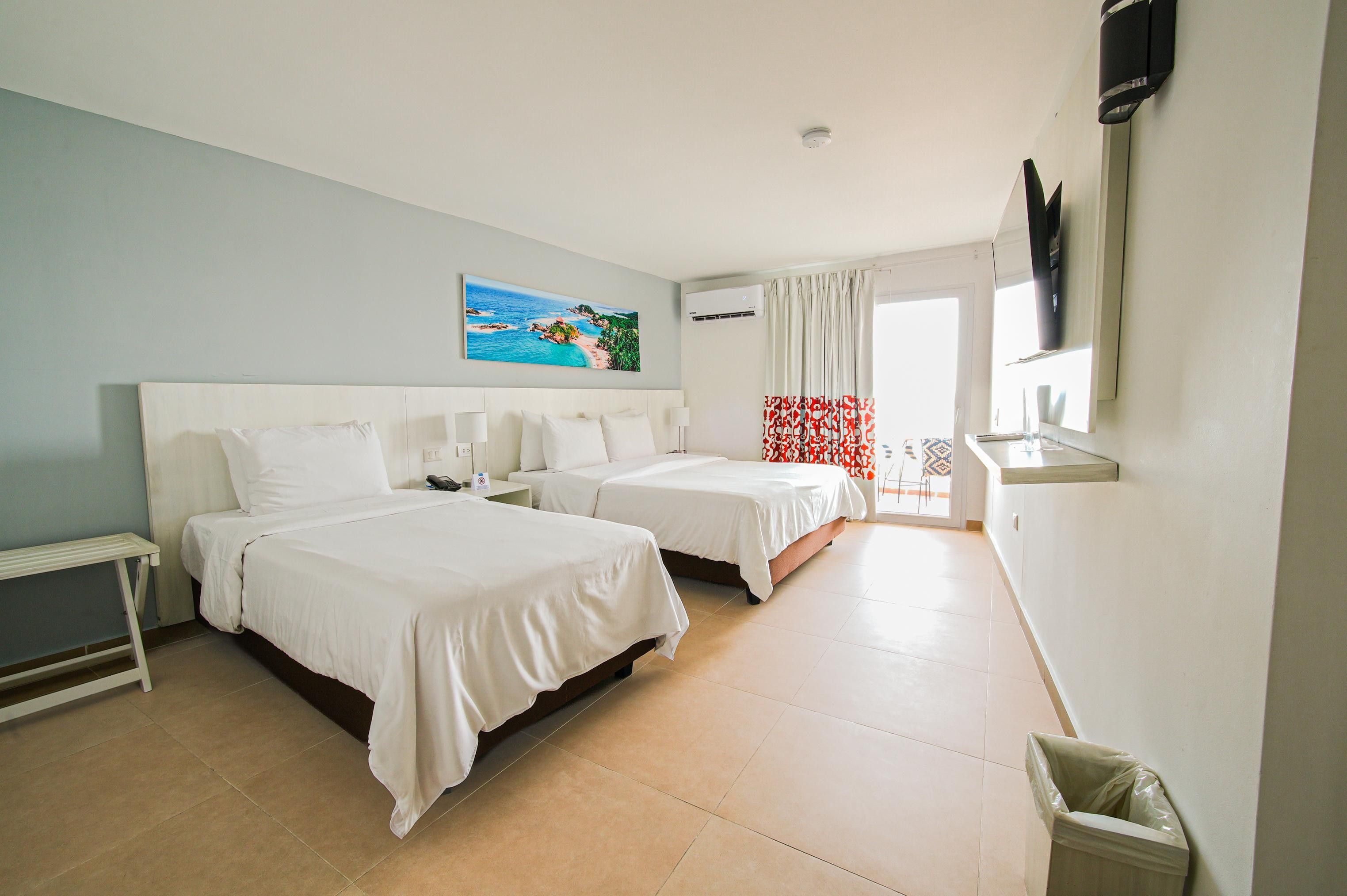 Une chambre d’hôtel avec deux lits, un tableau, un appareil de climatisation, une fenêtre avec des rideaux et un téléviseur fixé au mur.