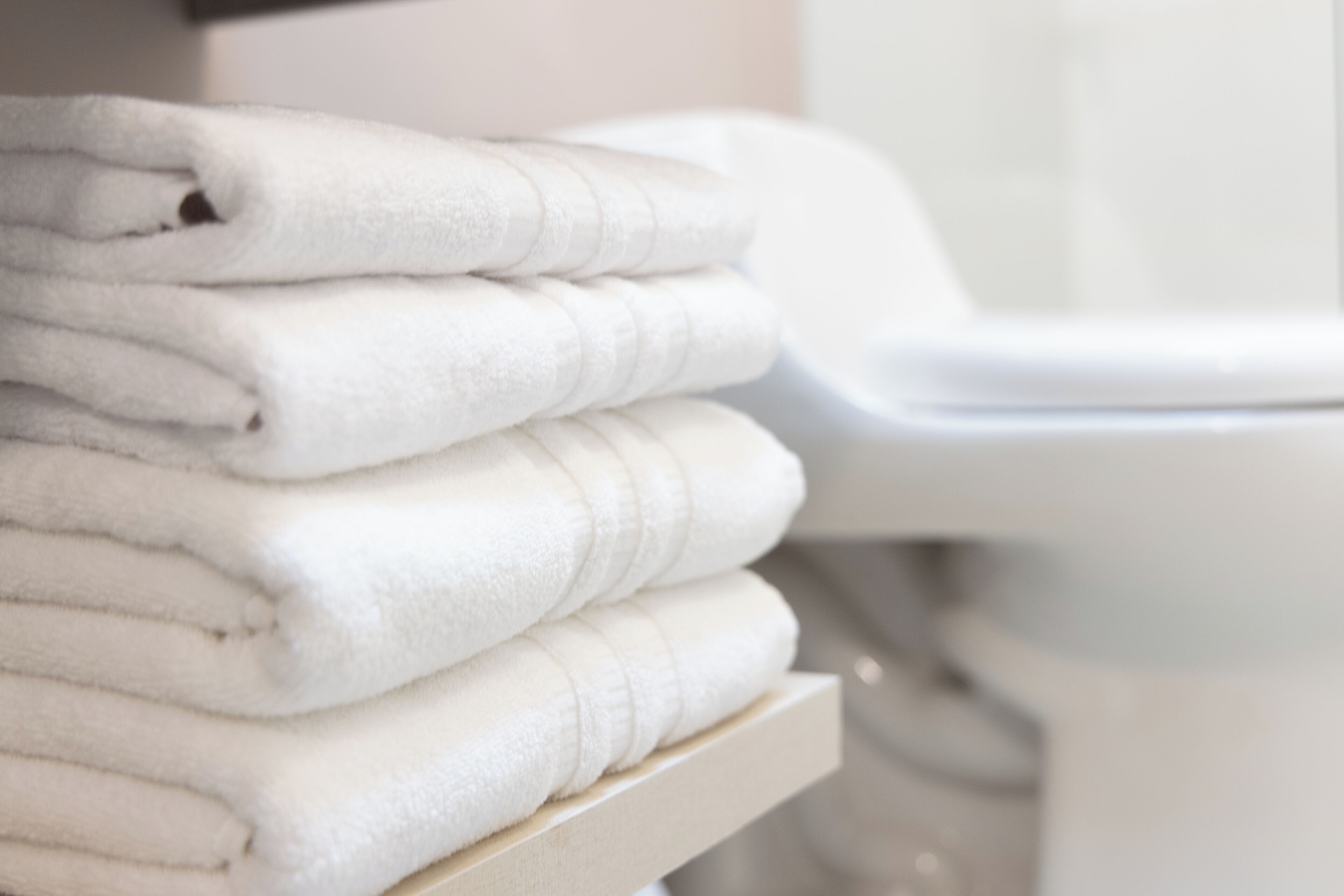 Una pila de toallas blancas sobre un estante de madera en un baño.