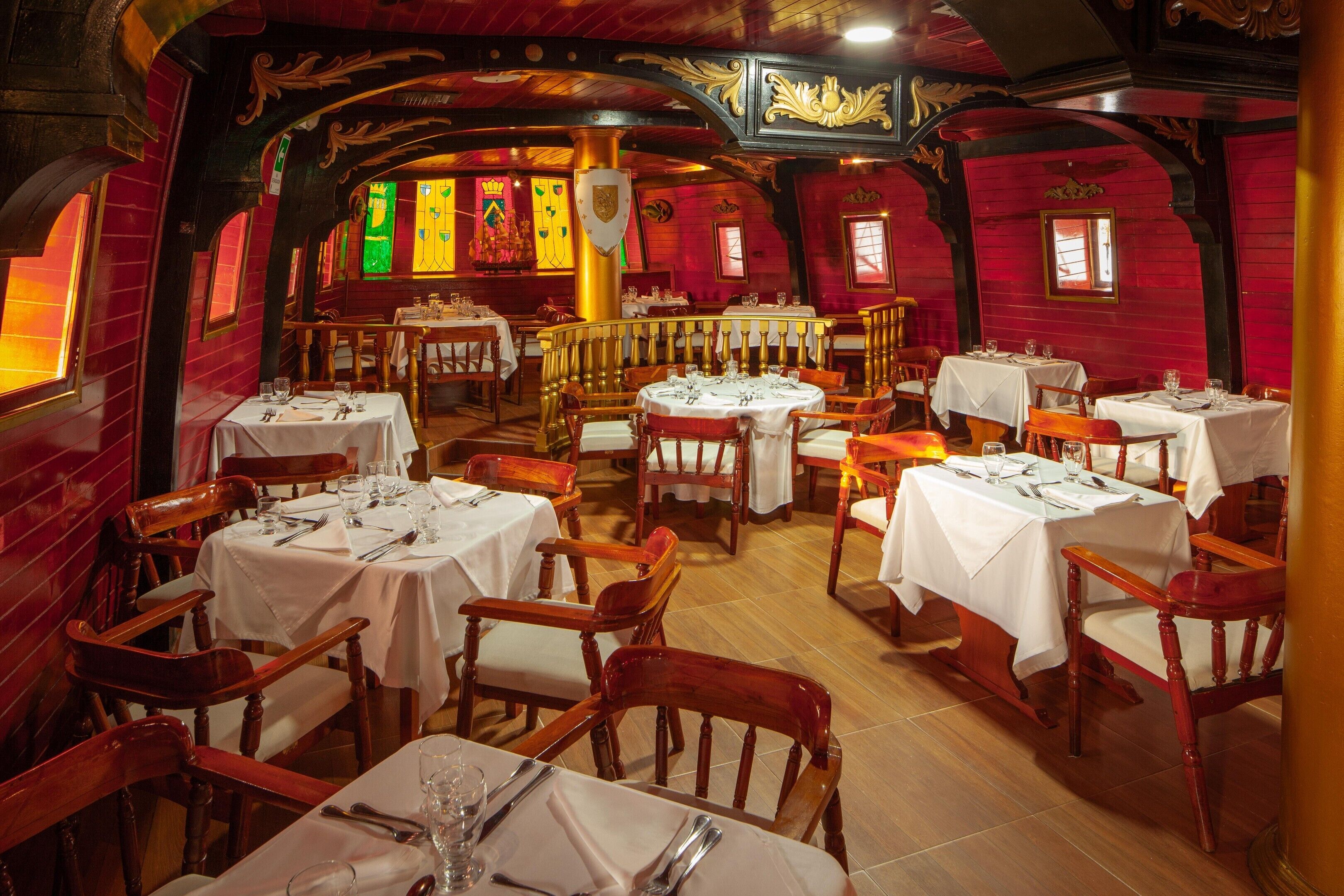 A restaurant with multiple tables and chairs, wooden beams, and stained glass windows.