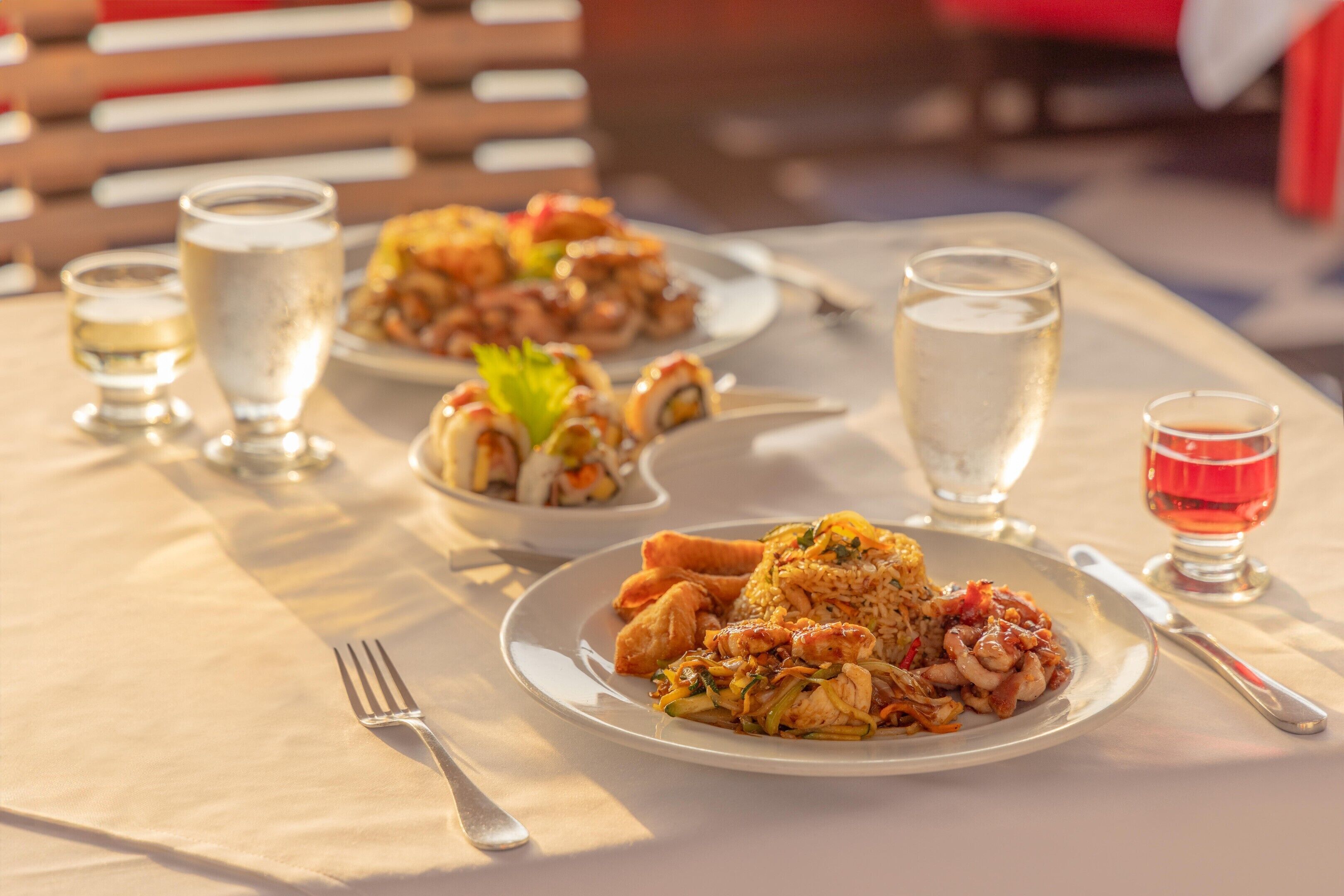 A table set with plates of food, glasses of water, and a glass of red wine.