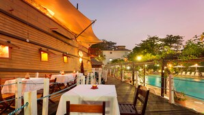 An outdoor dining area with tables and chairs, a pool, and a wooden deck.