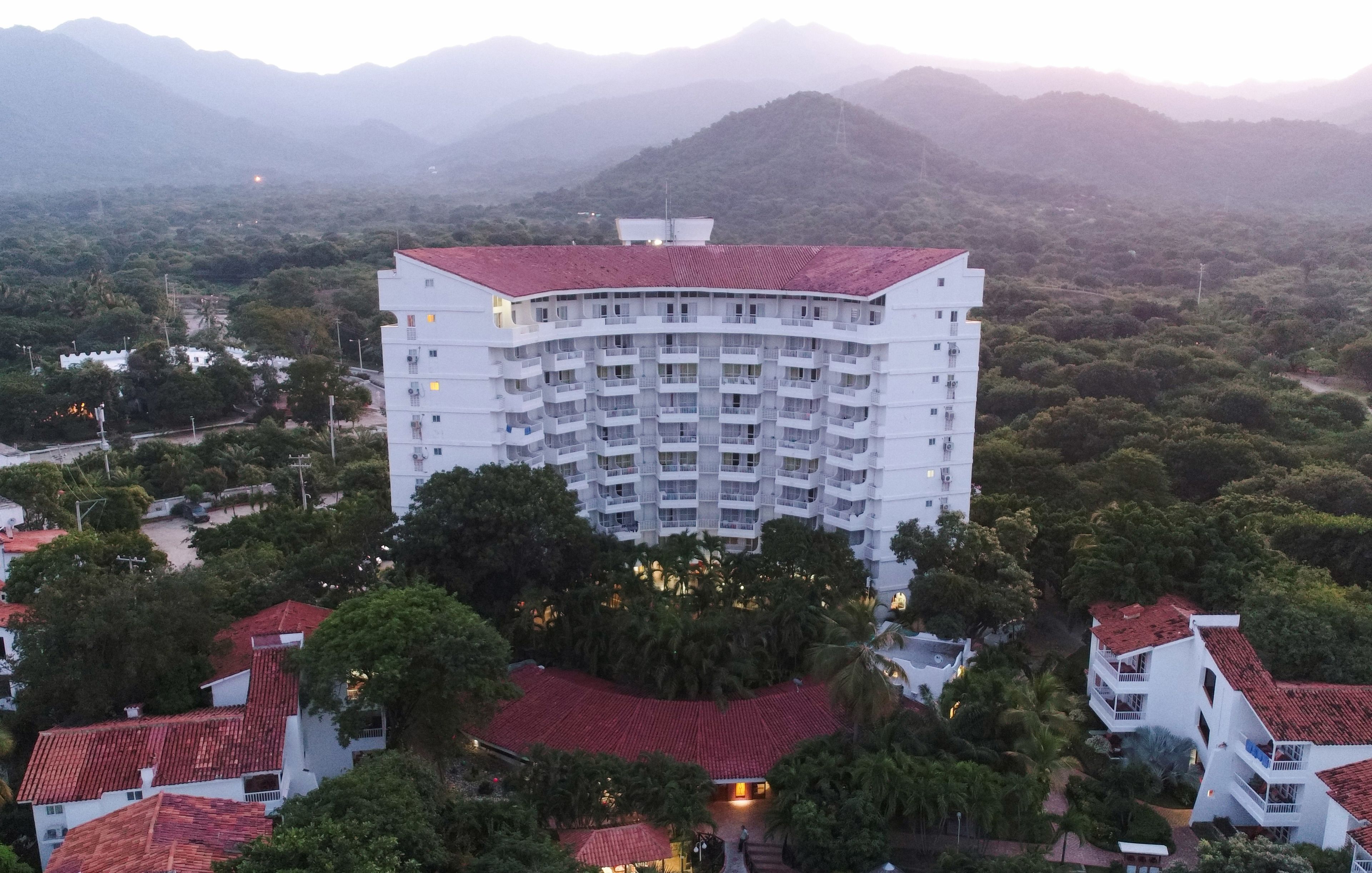 Un hotel de varios pisos con techo curvo, rodeado de abundante vegetación y montañas al fondo.
