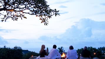 Un grupo de personas sentadas en sofás al aire libre junto a una piscina al anochecer.