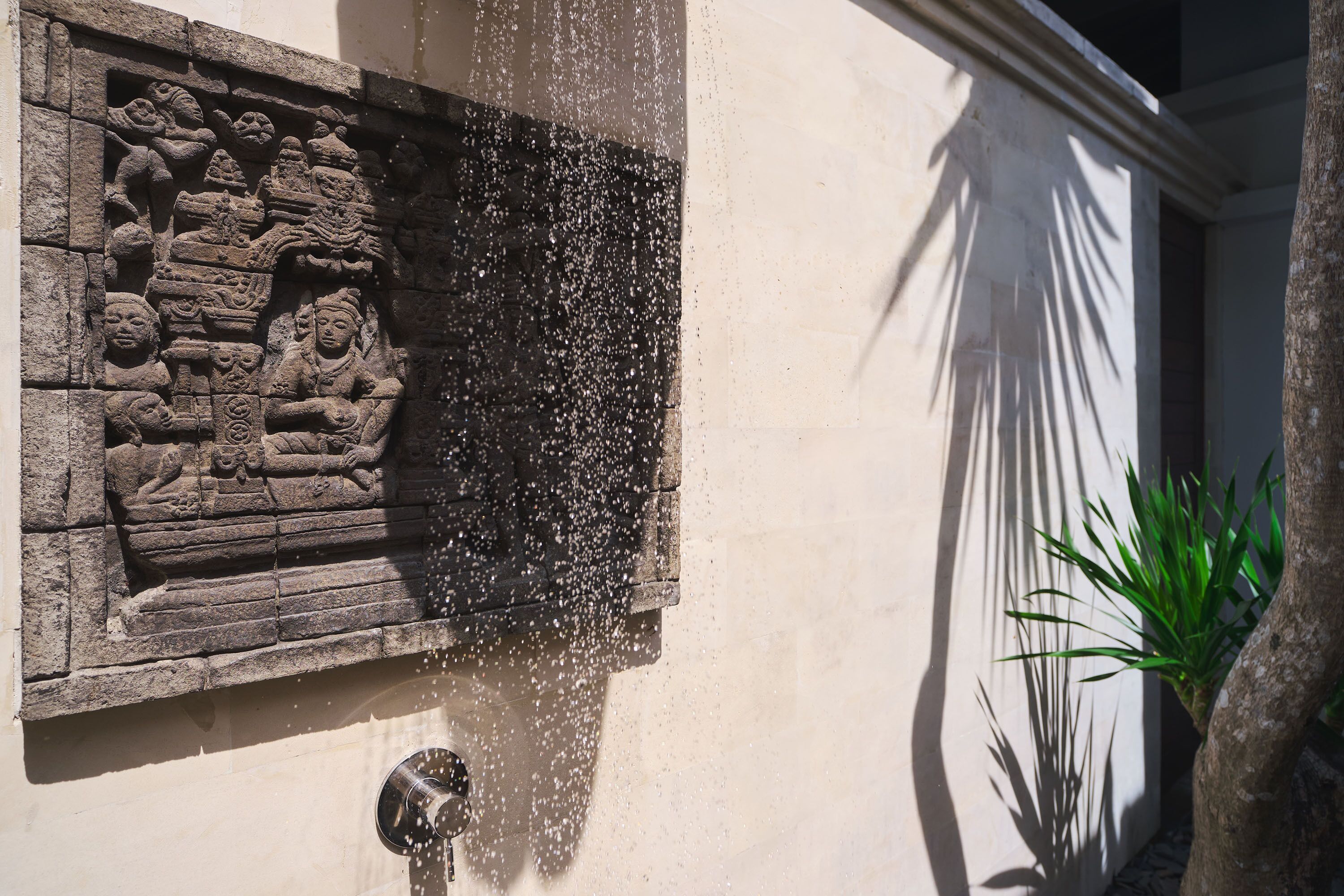 A stone relief sculpture on a building wall with water spraying from a nearby source.
