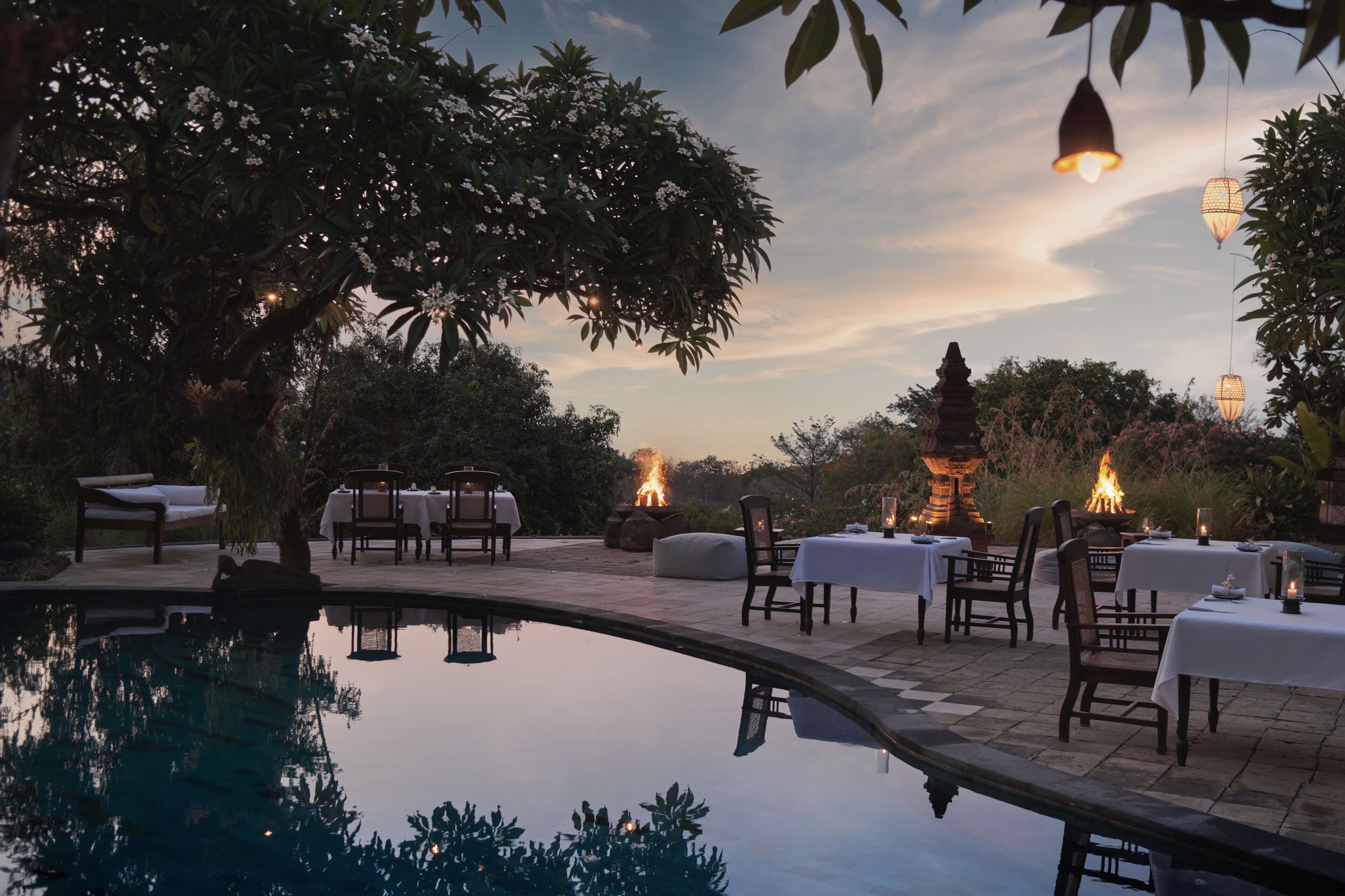 An outdoor dining area with tables and chairs, a fire pit, and a pool.