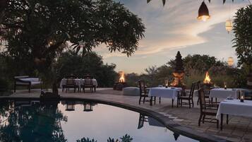 An outdoor dining area with tables and chairs, a fire pit, and a pool.