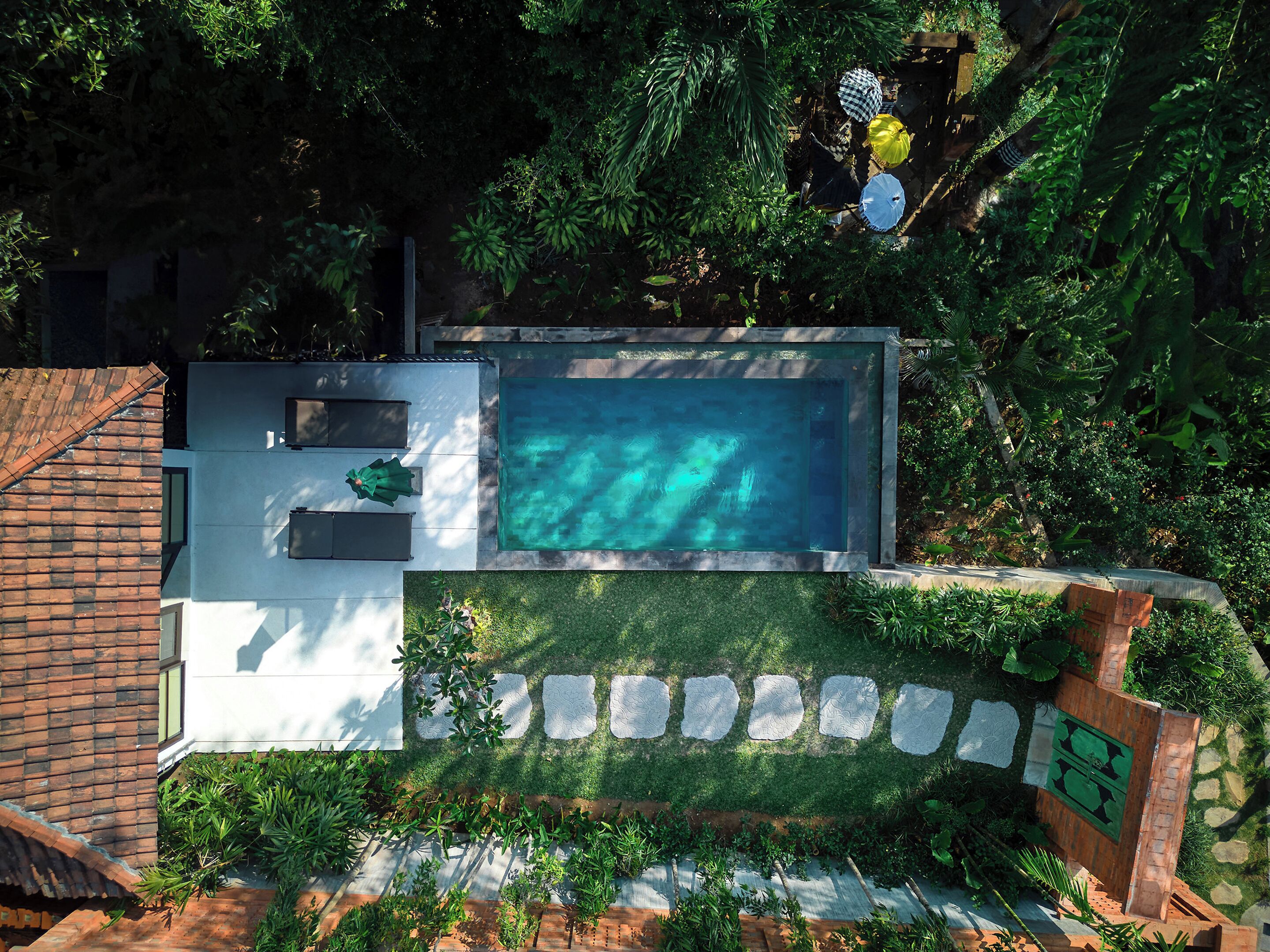 An aerial view of a backyard with a swimming pool, a patio area, and surrounding greenery.