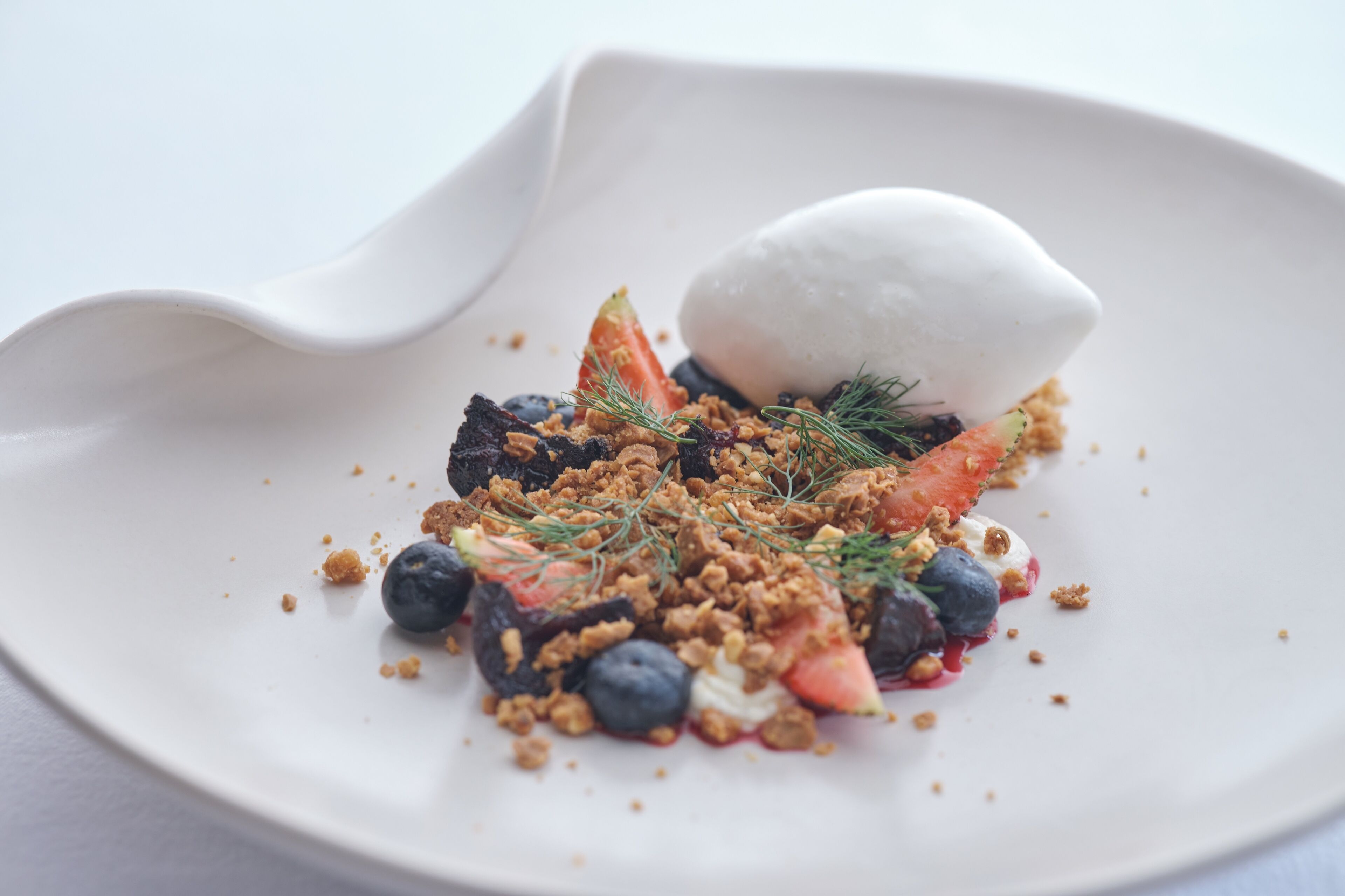 Un plat blanc amb un postre fet de baies, granola i una culleradeta de gelat.
