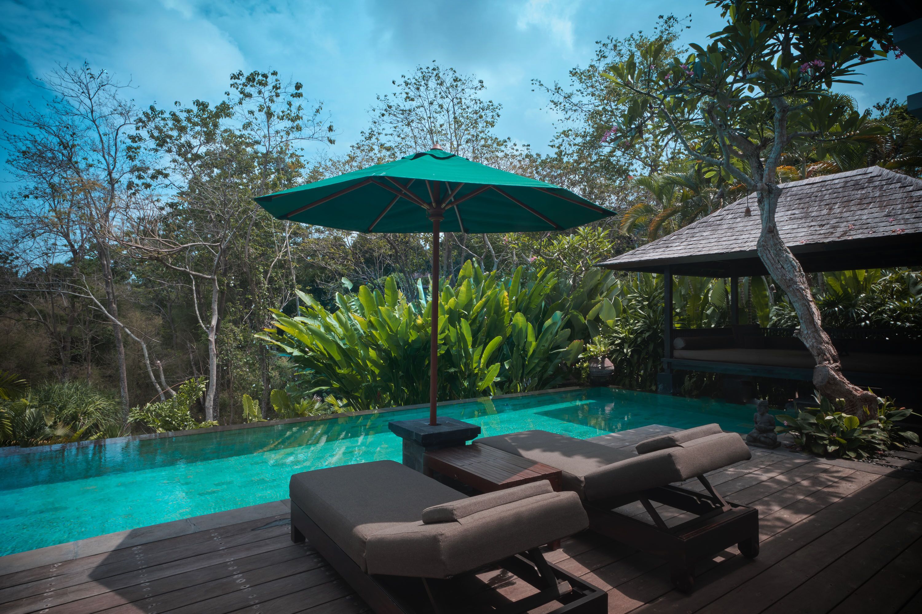 Uma área à beira da piscina com espreguiçadeiras e um guarda-sol verde.