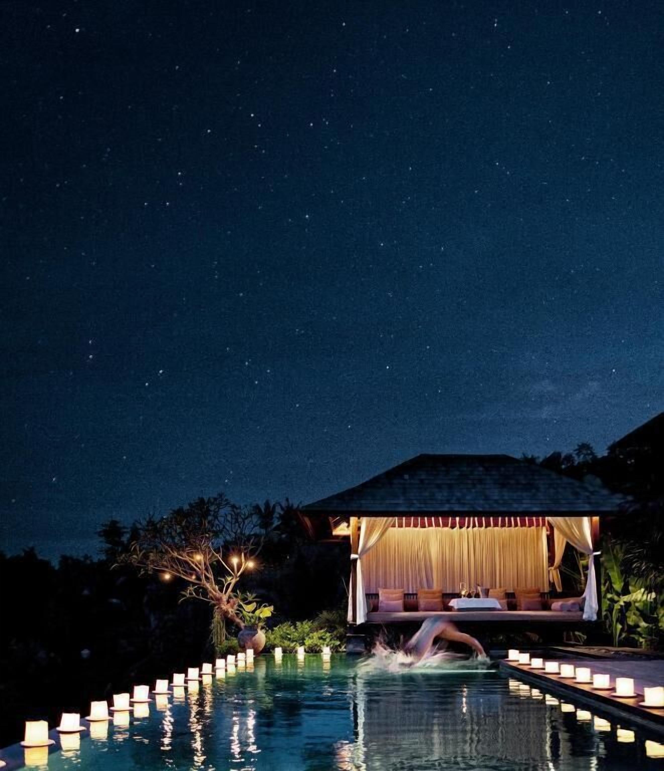A nighttime pool area with a covered seating area and candles along the edge.