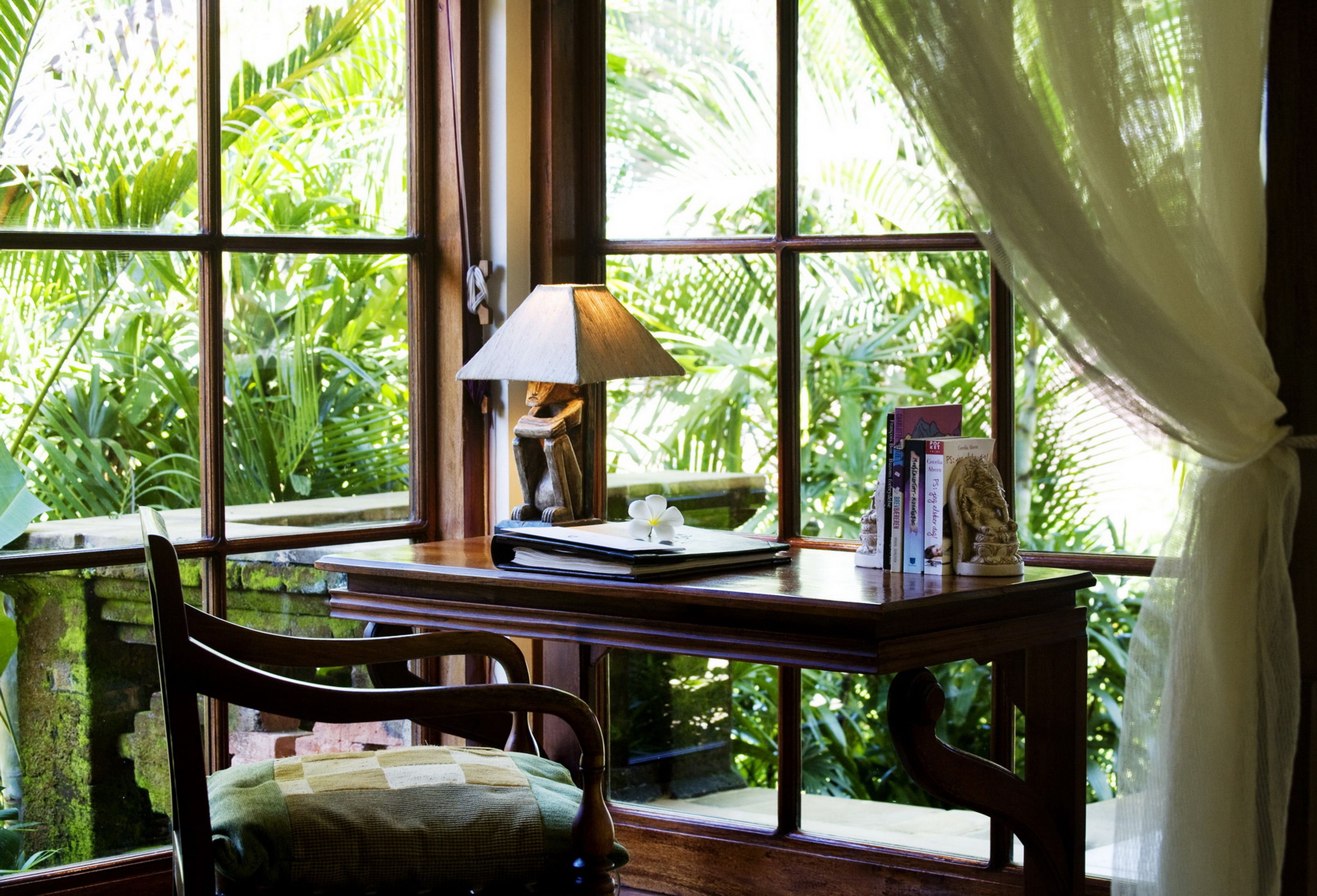 A room with a large window, a wooden desk, a chair, and a lamp.