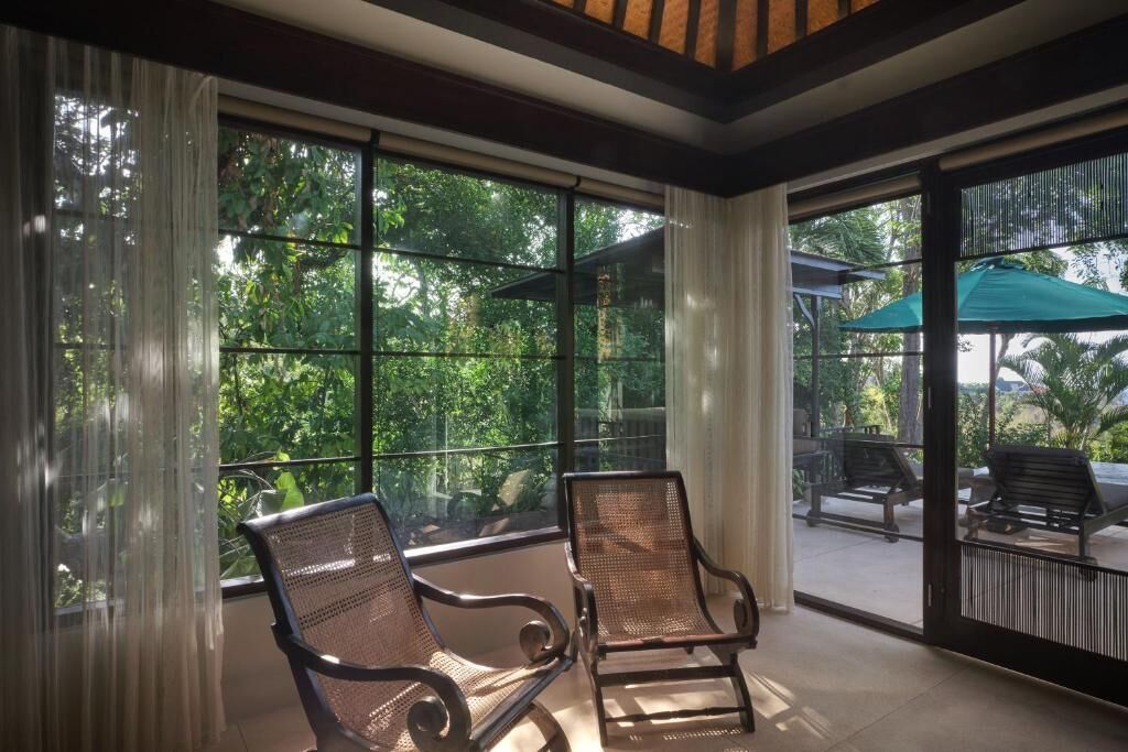 Una habitación con ventanas amplias, sillas de mimbre y un patio exterior con una sombrilla verde.