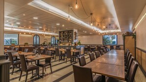 Un restaurante espacioso con techos altos, iluminación colgante y una larga mesa común.