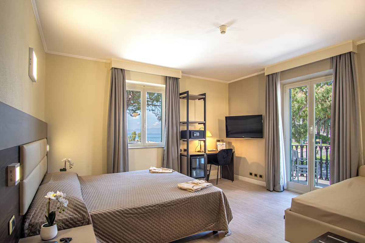 A hotel room with a bed, desk, chair, TV, and a balcony with a view.