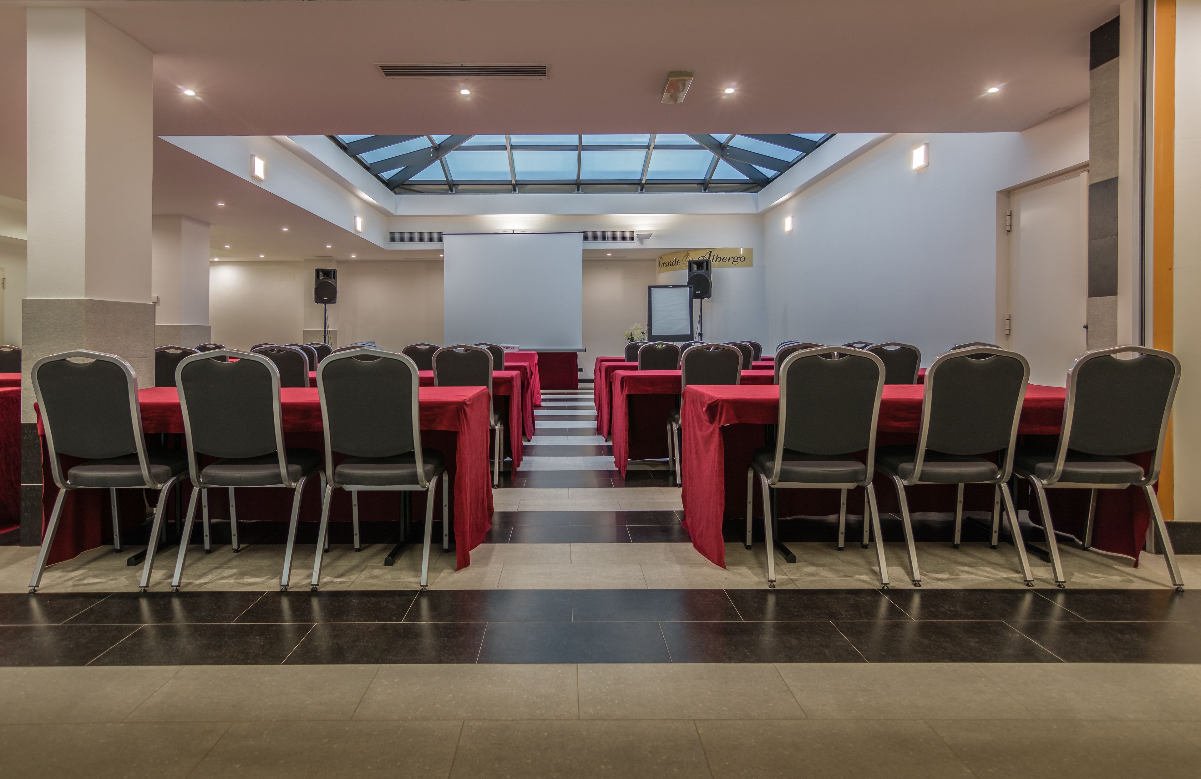 A conference room with a high ceiling, skylight, and a stage with a projector screen.