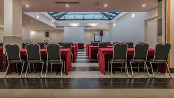 A conference room with a high ceiling, skylight, and a stage with a projector screen.