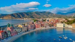 Un pueblo costero con edificios coloridos a lo largo de la costa, barcos en el agua y montañas al fondo.