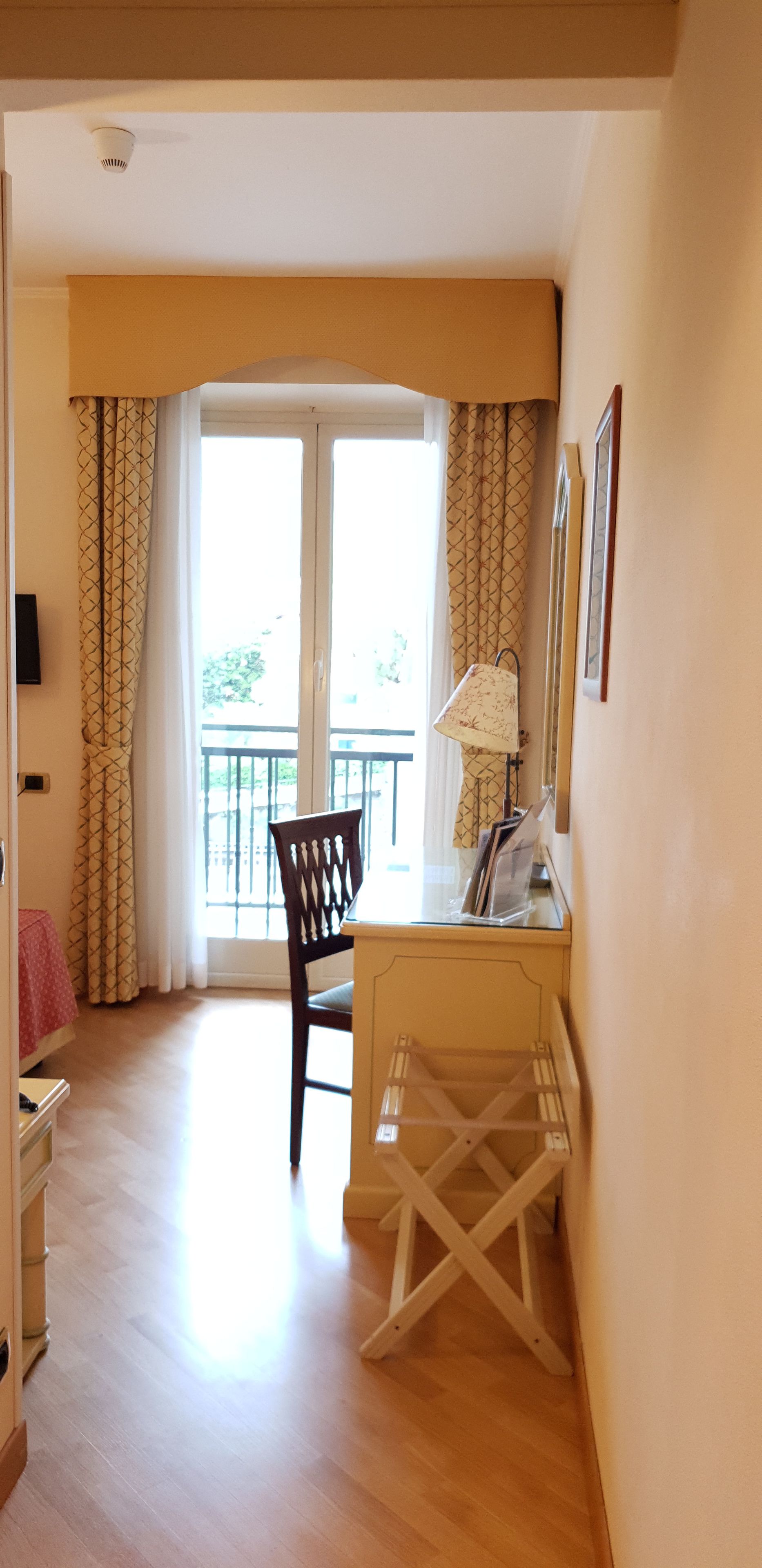 Habitación con escritorio, silla y vistas al balcón exterior por una puerta corrediza de vidrio.