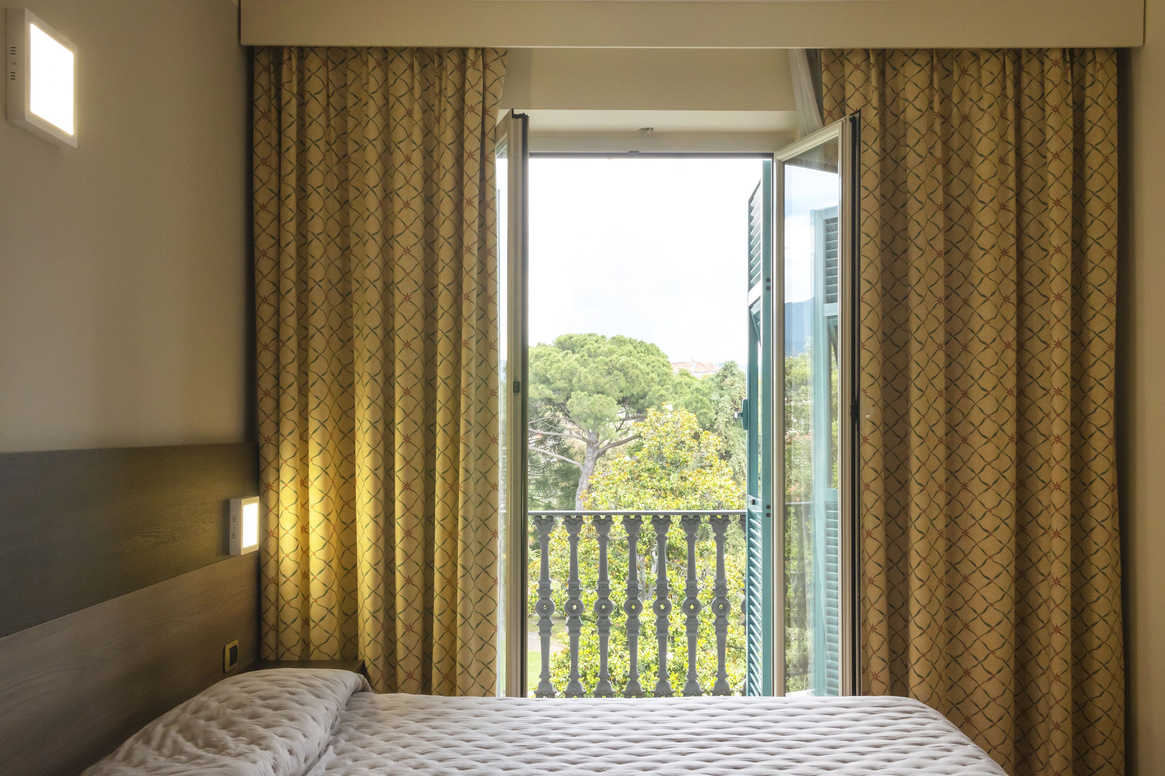 Une chambre d’hôtel avec un lit, une fenêtre avec des rideaux et une vue sur les arbres à l’extérieur.