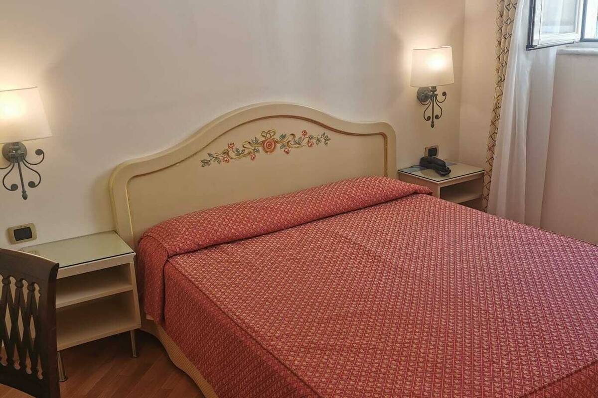 A bedroom with a bed, a desk, a chair, and two bedside lamps.