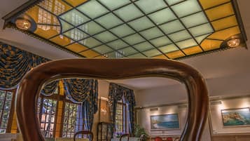 Una sala imponente con un techo de vitrales grande, muebles de madera ornamentados y vistas al exterior a través de amplias ventanas.