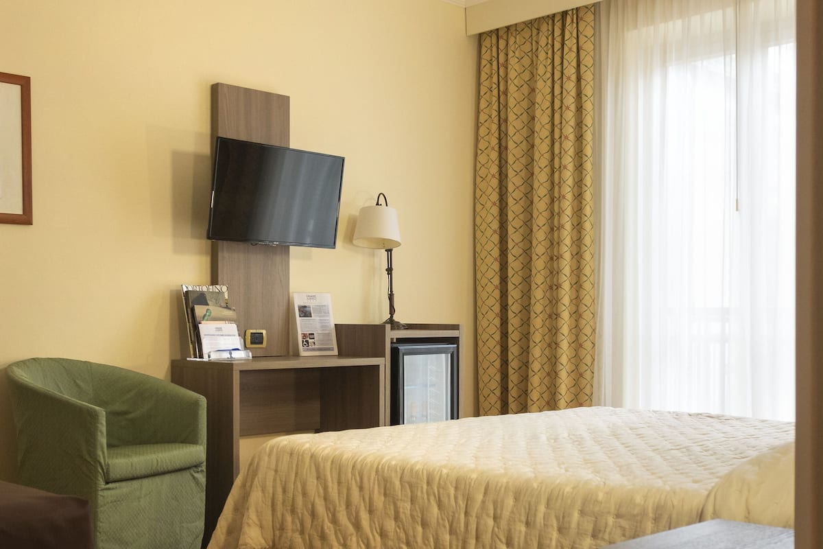 A hotel room with a bed, a desk with a computer, a television, and a green armchair.