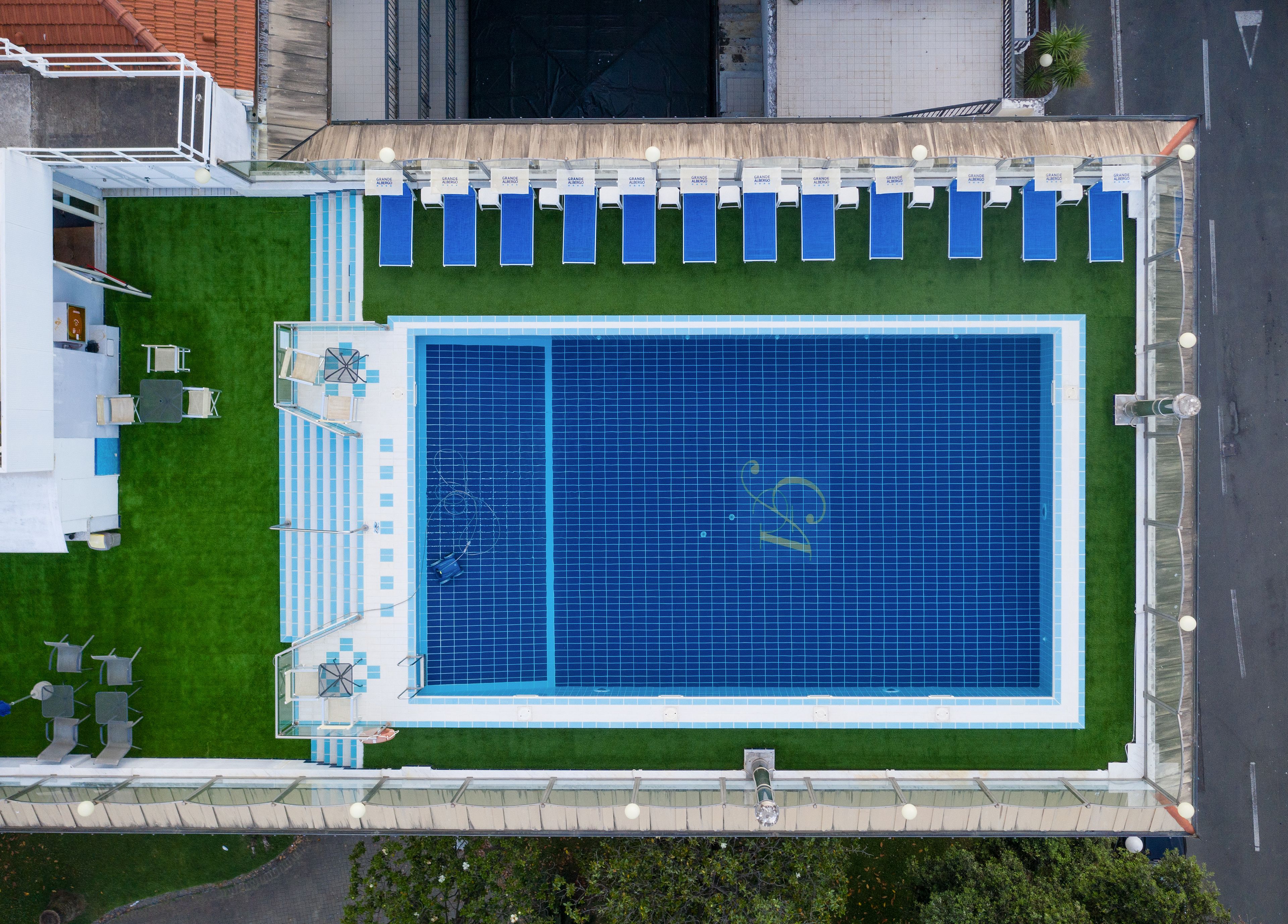 An aerial view of a swimming pool with blue tiles, surrounded by a green lawn and a row of blue chairs.