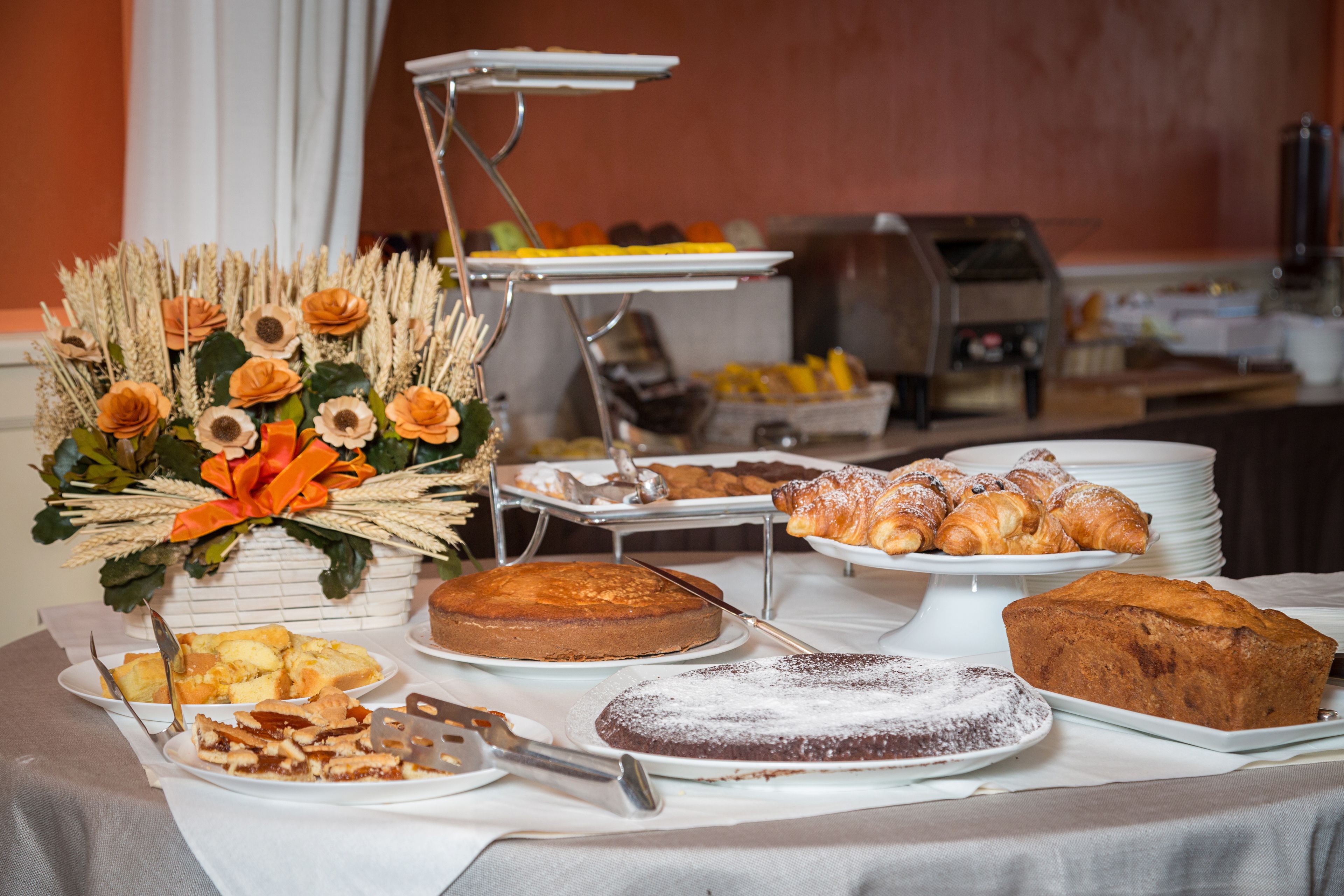 En buffetbord med et udvalg af desserter og kager, herunder kager, tærter og en dekorativ blomsteropsætning.