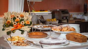 En buffetbord med et udvalg af desserter og kager, herunder kager, tærter og en dekorativ blomsteropsætning.