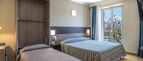 A hotel room with two beds, a wardrobe, a nightstand with a lamp, and a window with curtains.