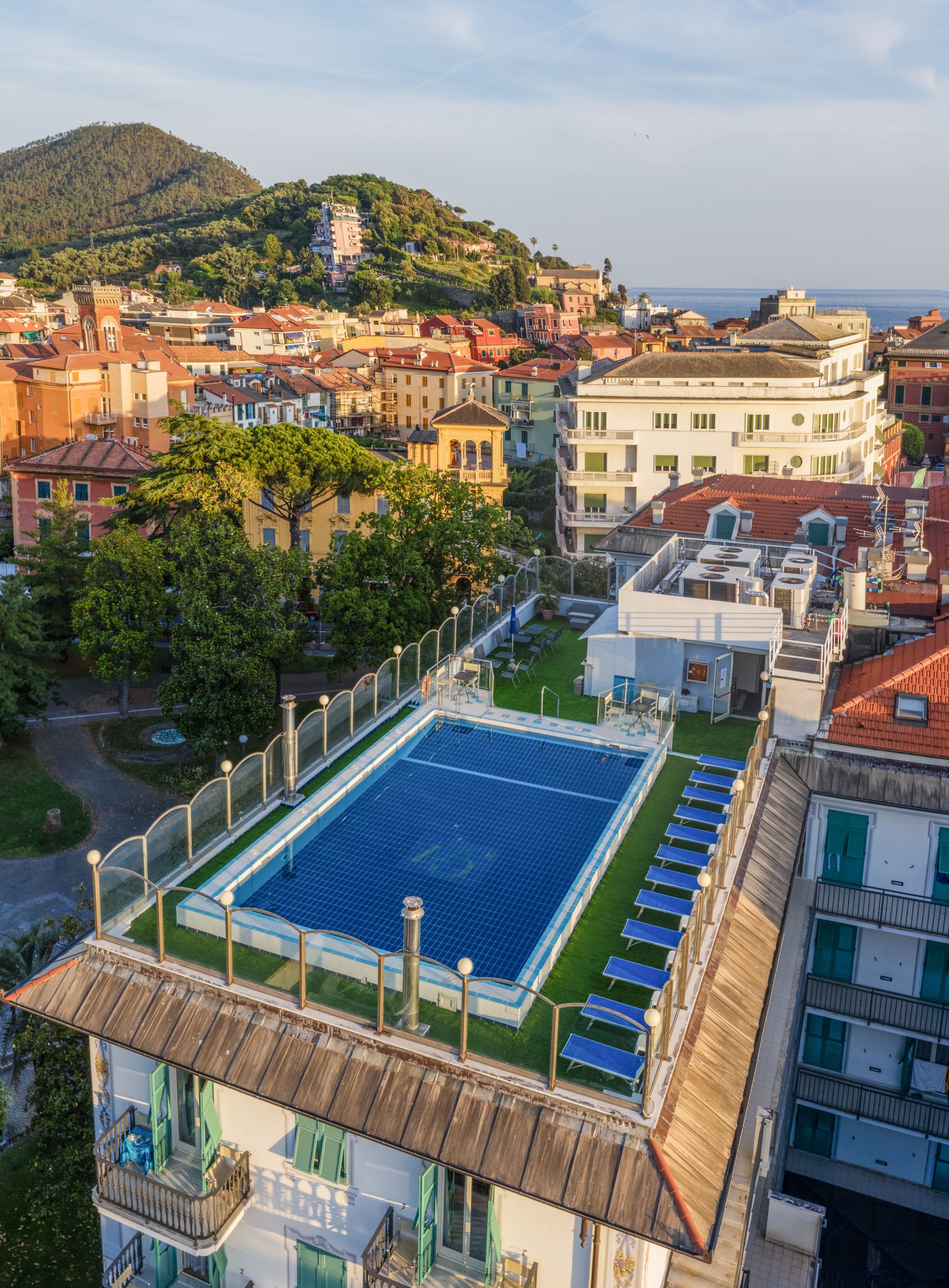 Une piscine sur le toit, dotée de panneaux solaires, entourée d’immeubles avec balcons et avec une colline en arrière-plan.