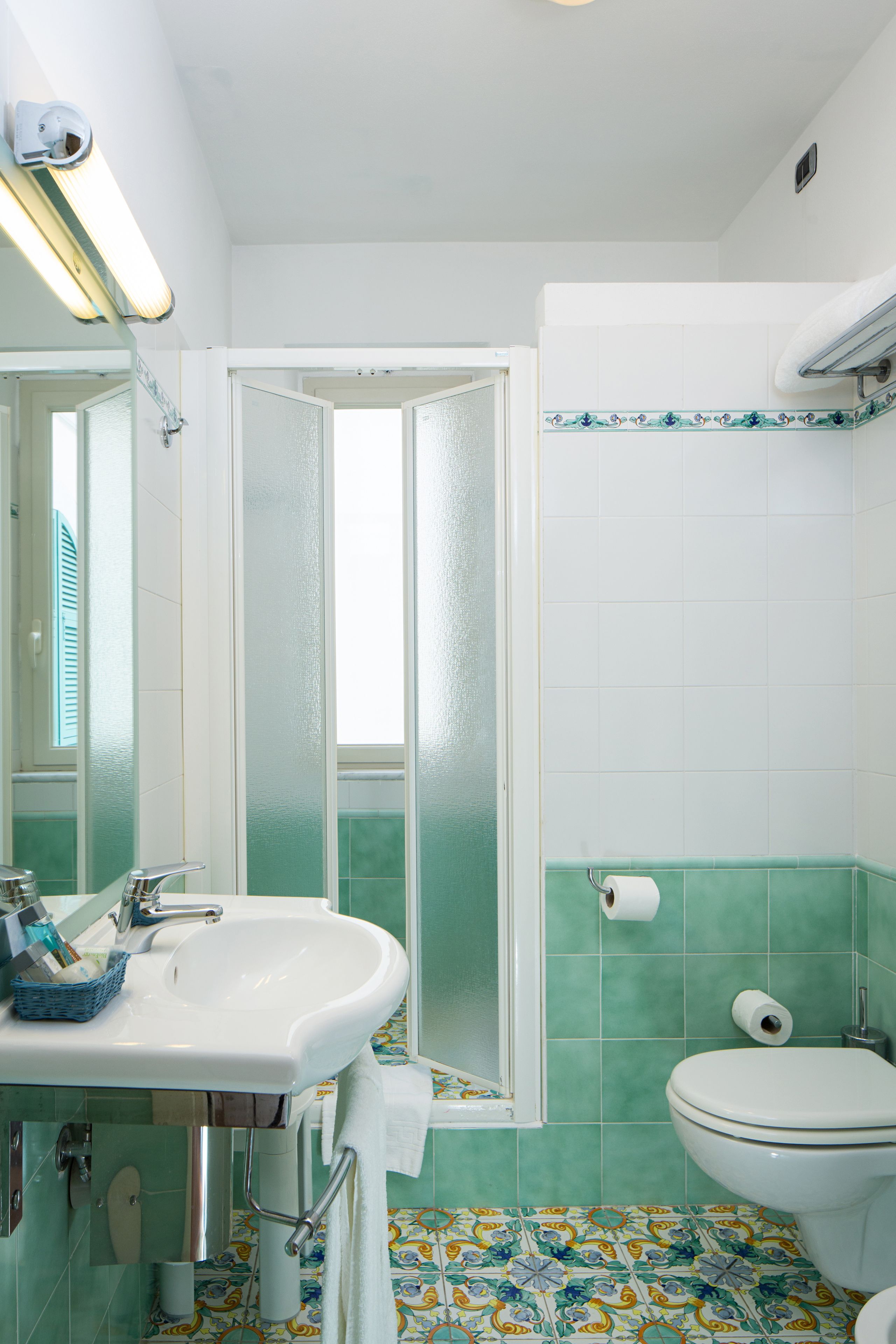A bathroom with a white sink, toilet, and shower. The walls are tiled with a green pattern, and there is a mirror above the sink.
