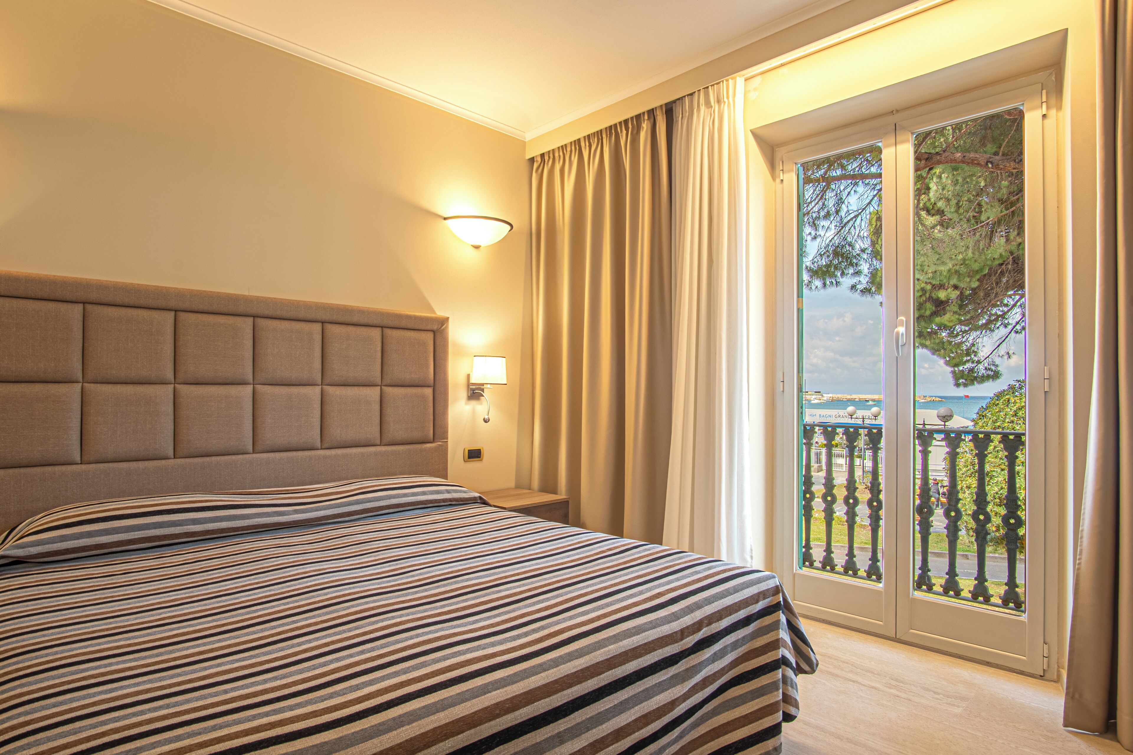 Une chambre d’hôtel avec un grand lit, une table de chevet, une lampe fixée au mur et une vue sur l’extérieur grâce à une porte-fenêtre coulissante.