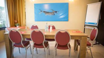 Un salón de conferencias con una mesa de madera, sillas rojas, un cuadro de un pez, una pizarra y una ventana con cortinas.
