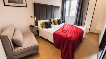 A hotel room with a bed, a sofa, a bedside table with a phone, and a window with curtains.