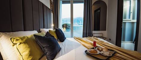 A hotel room with a large bed, multiple pillows, a tray with breakfast items, and a view of the city through the window.