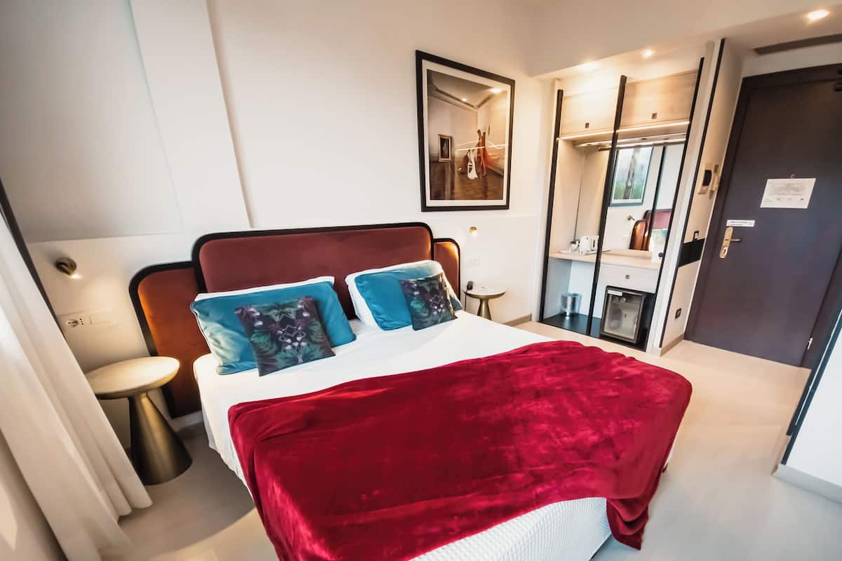 A modern hotel room with a large bed, a bedside table, a mirror, and a wardrobe.