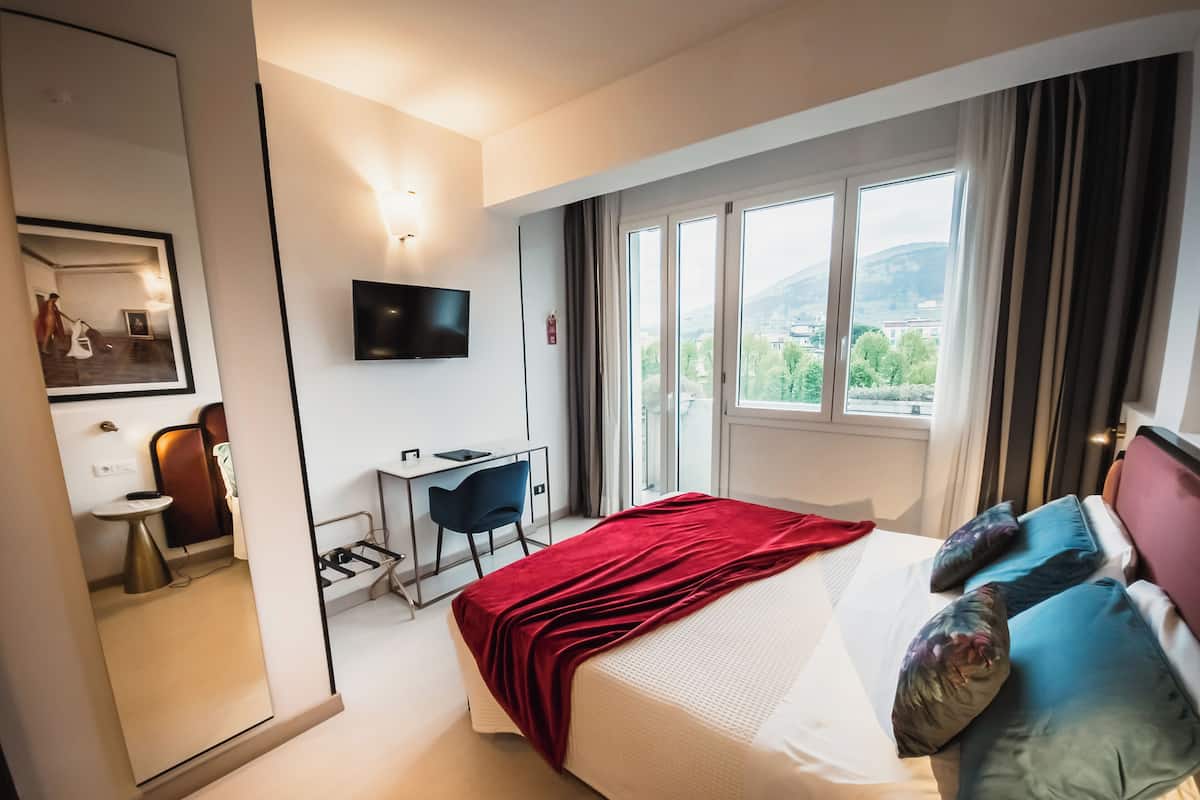 A hotel room with a bed, a desk, a chair, a TV, and a window with a view of the city.