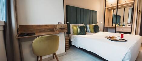 A modern hotel room with a bed, a desk, a chair, and a bedside table.