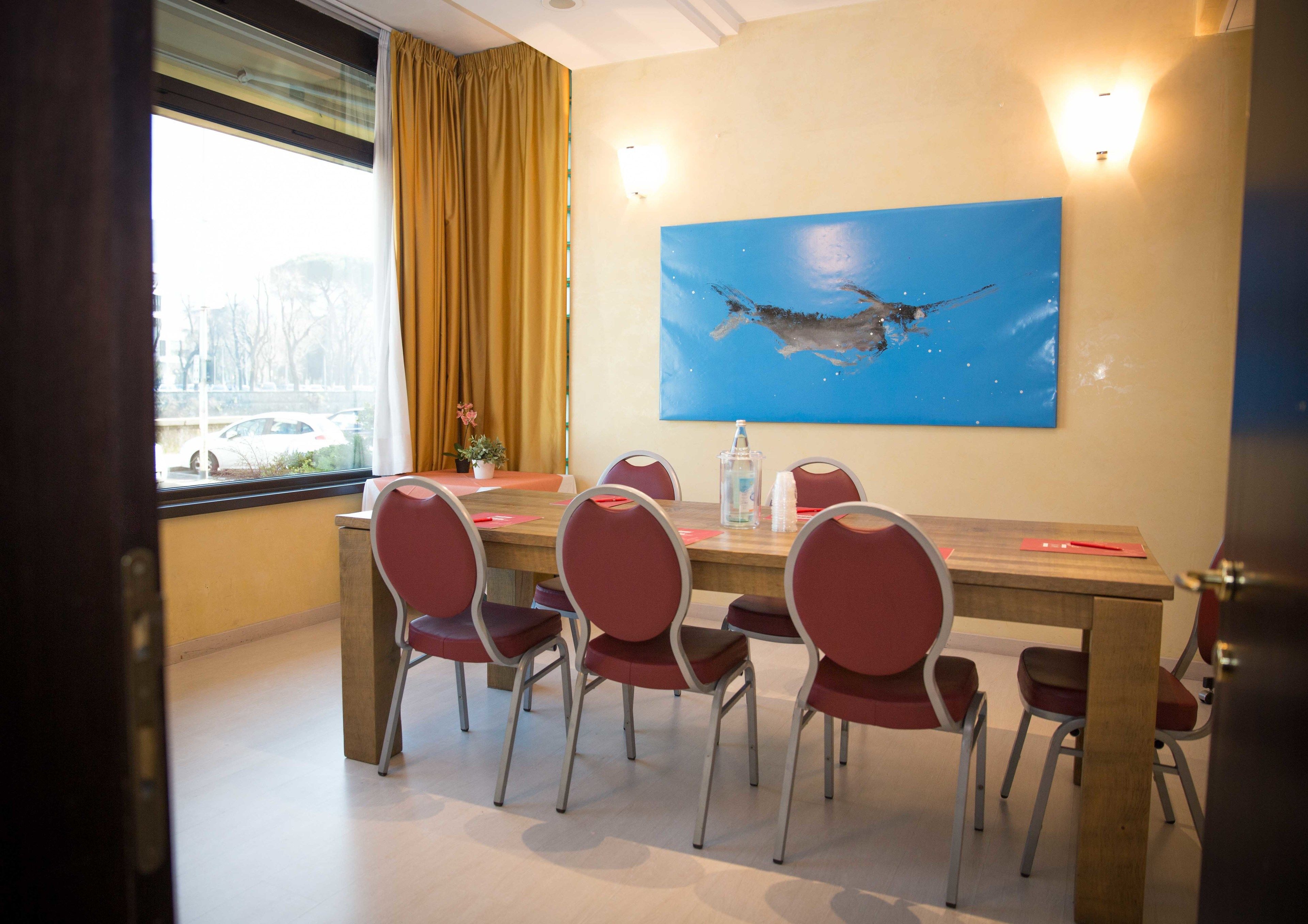 A conference room with a wooden table, six red chairs, a blue painting, and a window with curtains.