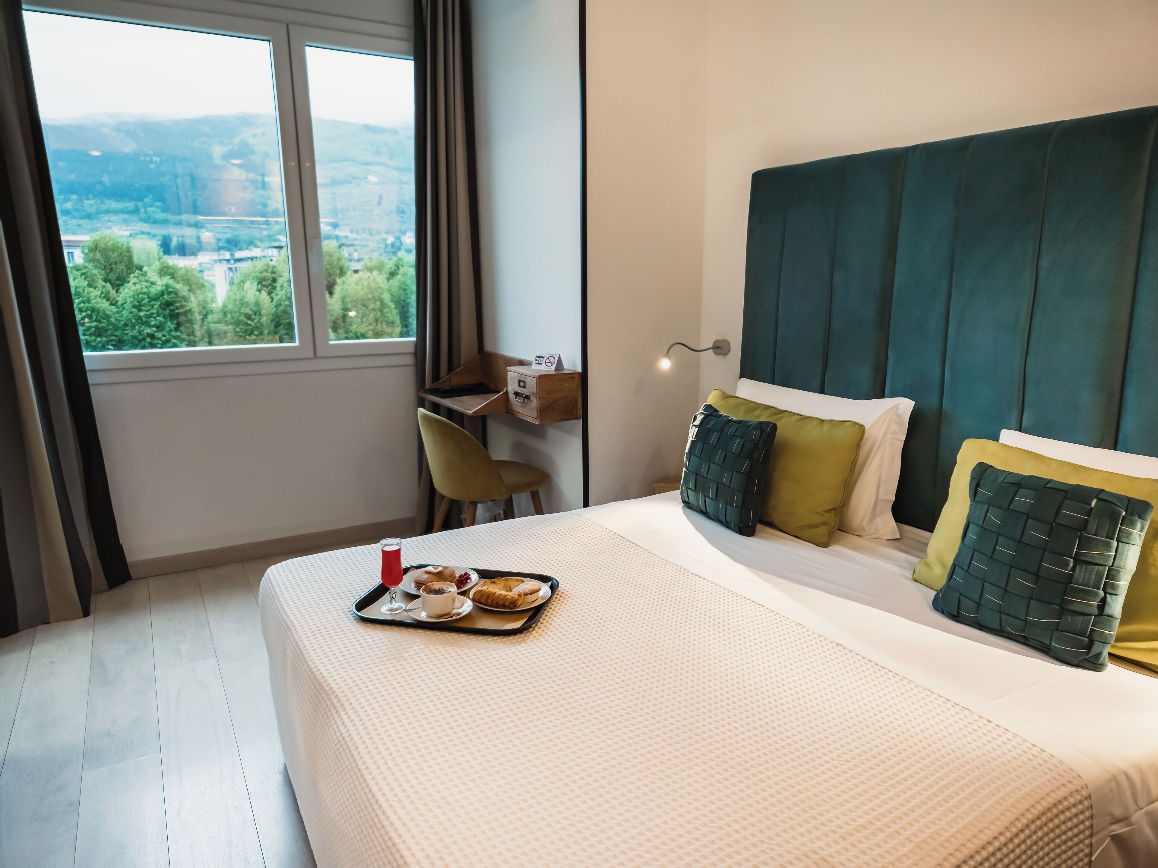 Ein Hotelzimmer mit Bett, Schreibtisch und Fenster mit Blick auf Grünflächen.